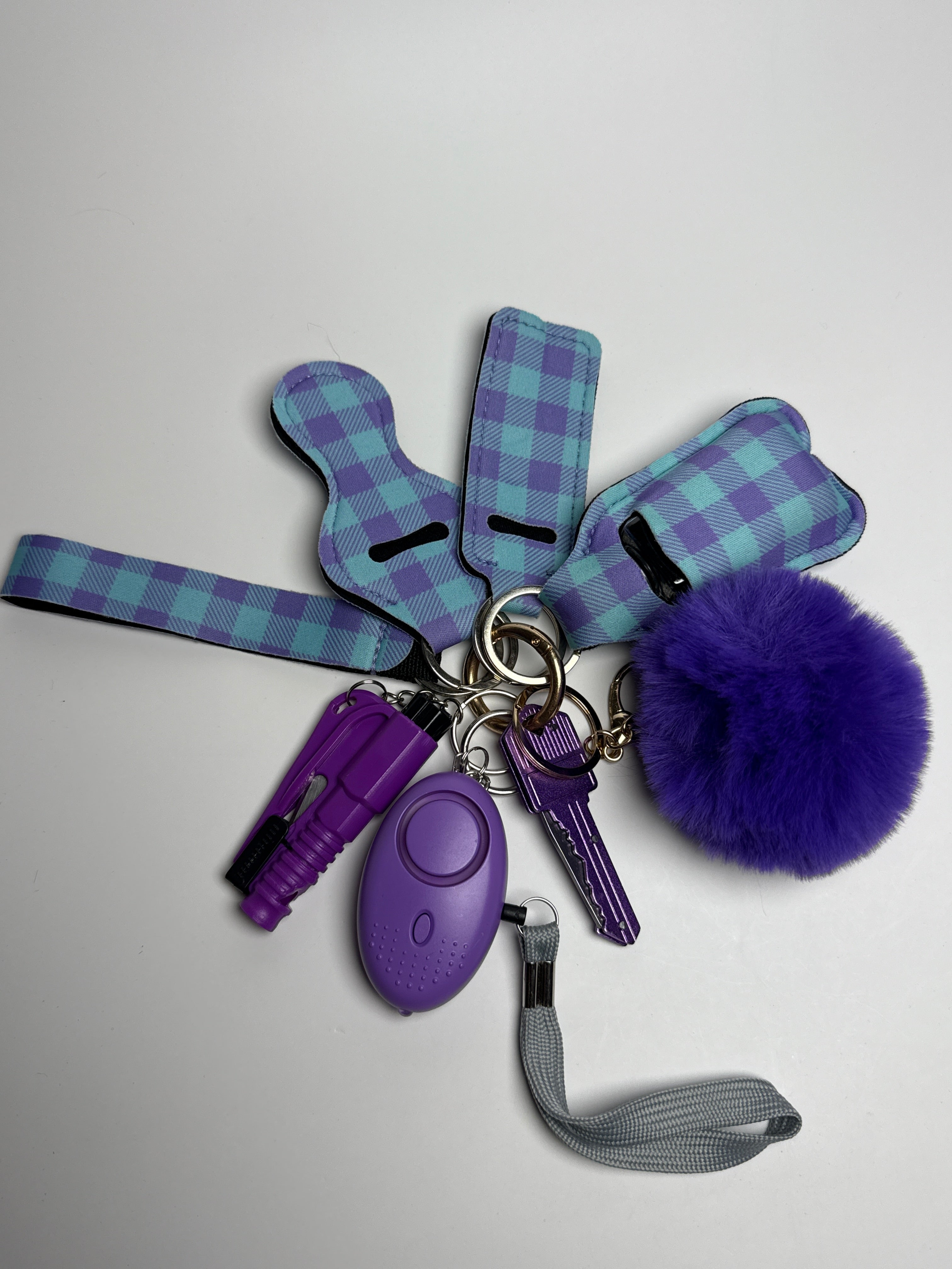 Blue plaid wristlet keychain set with purple pom charm, compact personal alarm, and mini light on a white background.