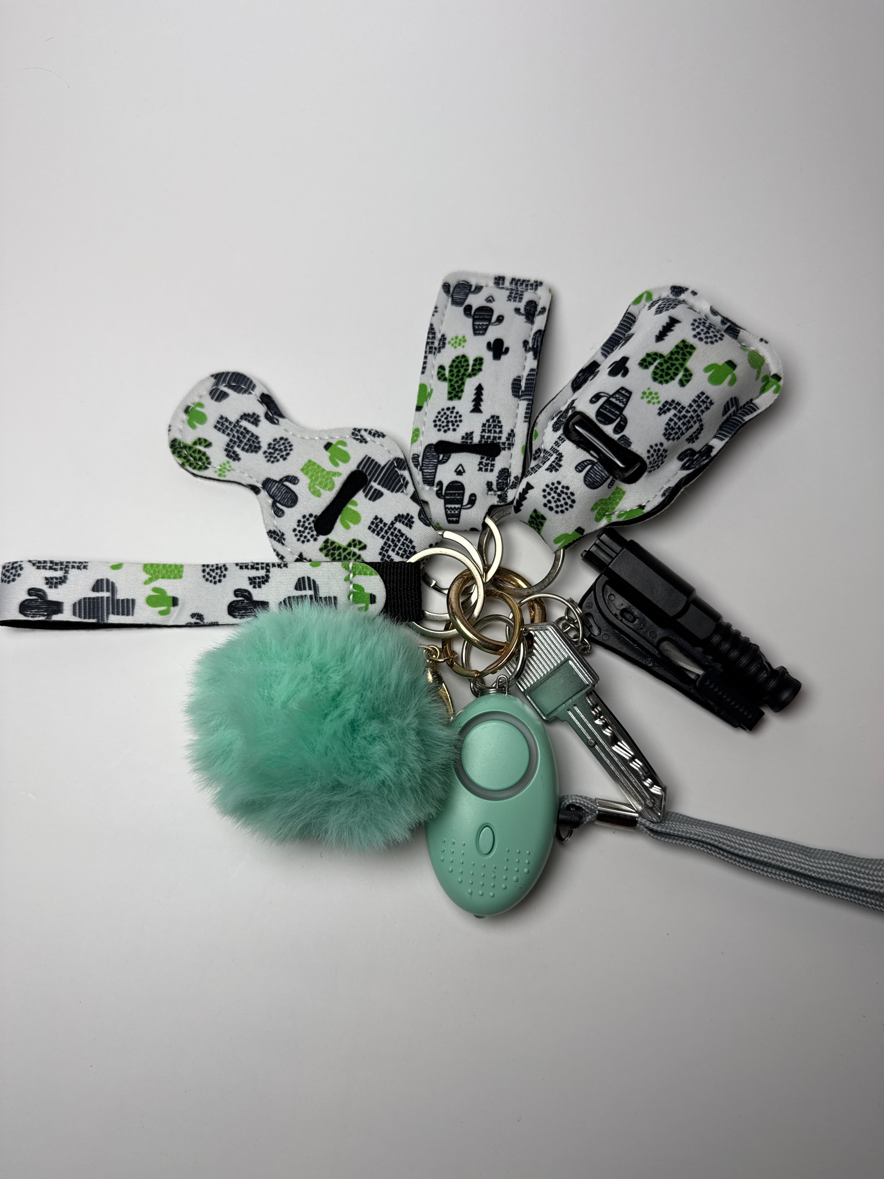 Cactus-print wristlet keychain set with mint pom charm, compact personal alarm, and mini light on a white background.