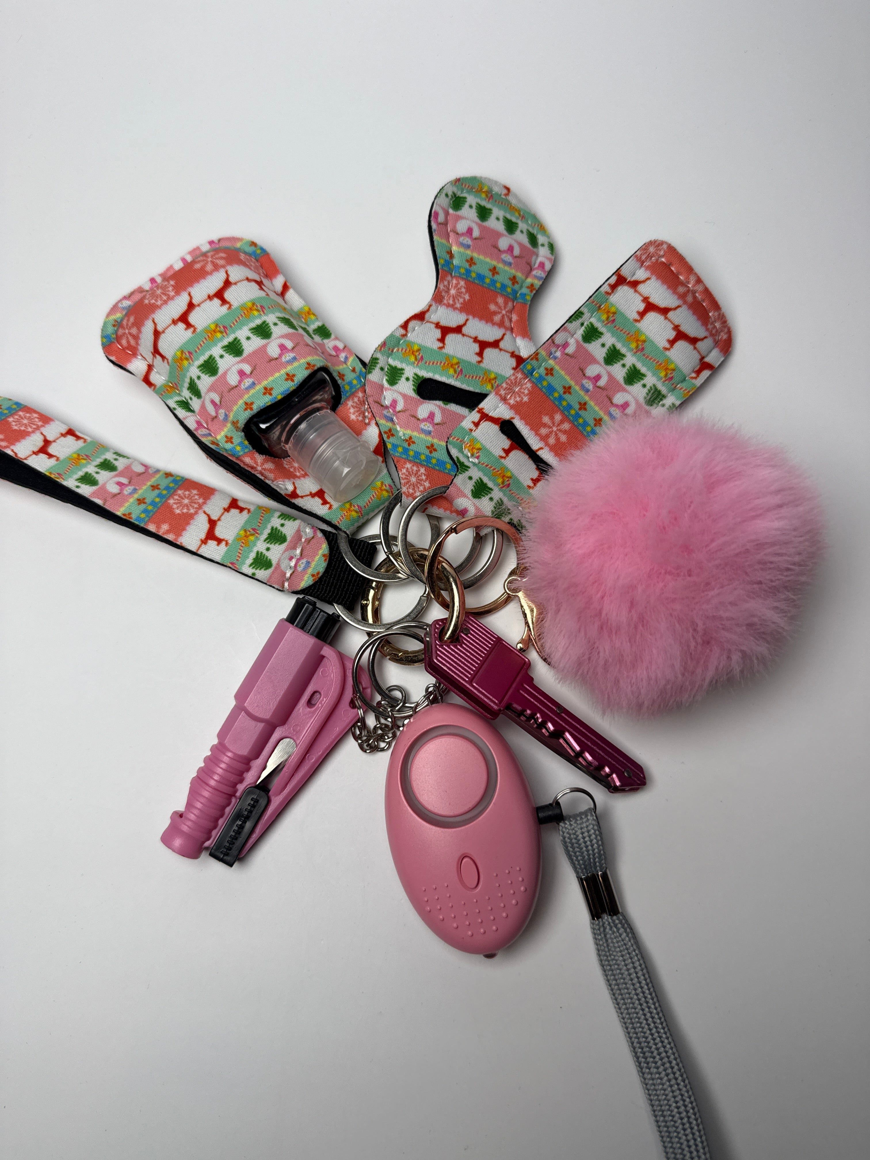 Patchwork holiday wristlet keychain set with pink pom charm, compact personal alarm, mini light, and clip-on bottle/holder on a white background.