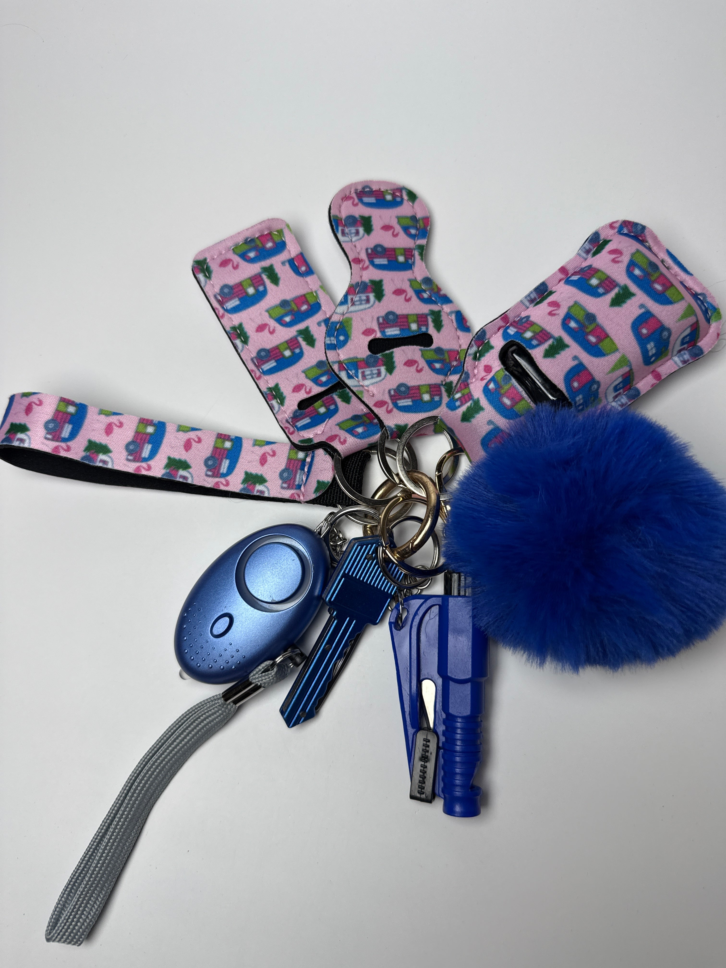 Camper-print wristlet keychain set with fluffy blue pom charm, compact personal alarm, and mini light on a white background.