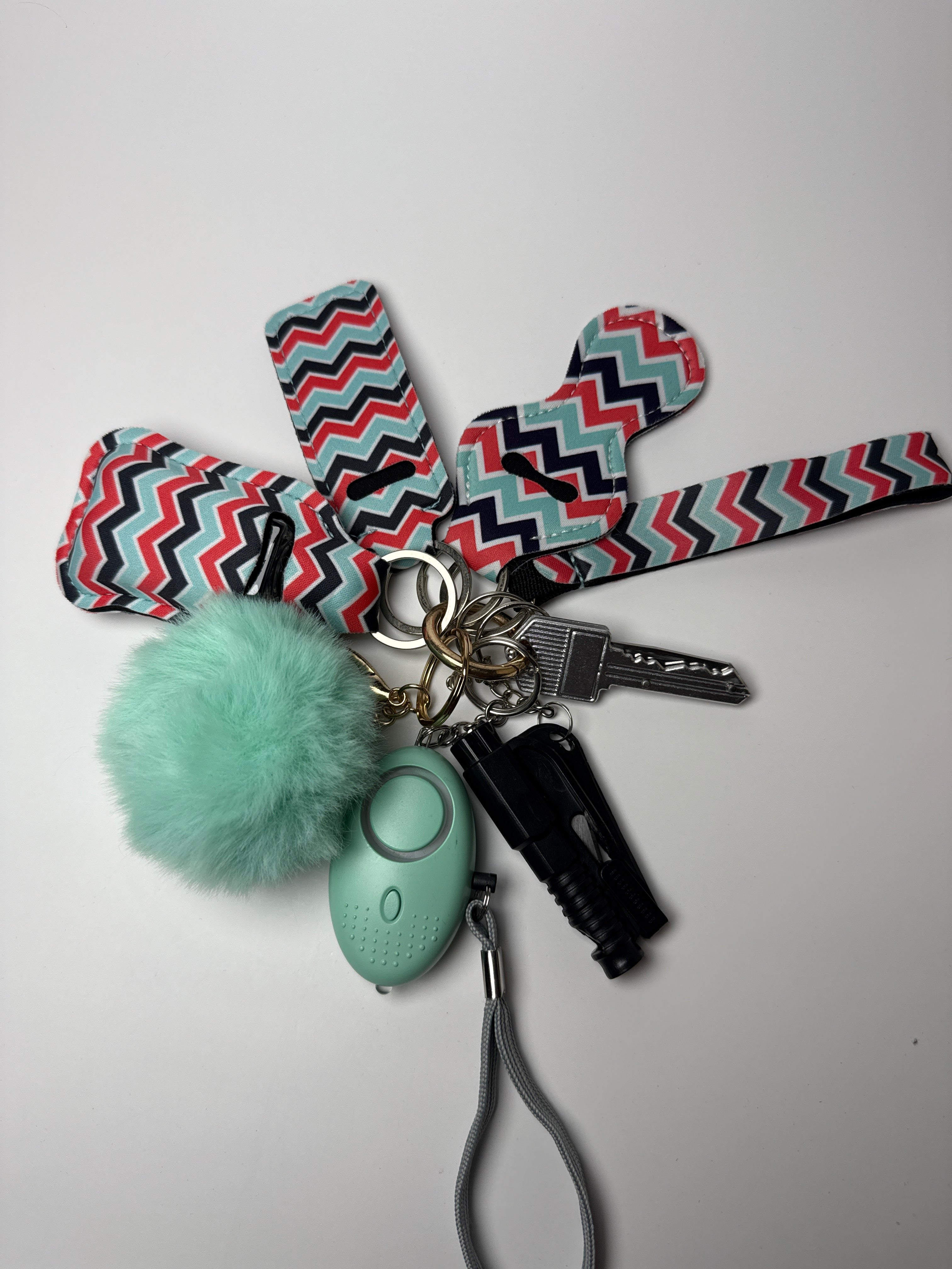 Multicolor zigzag wristlet keychain set with mint pom charm, compact personal alarm, and mini light on a white background.
