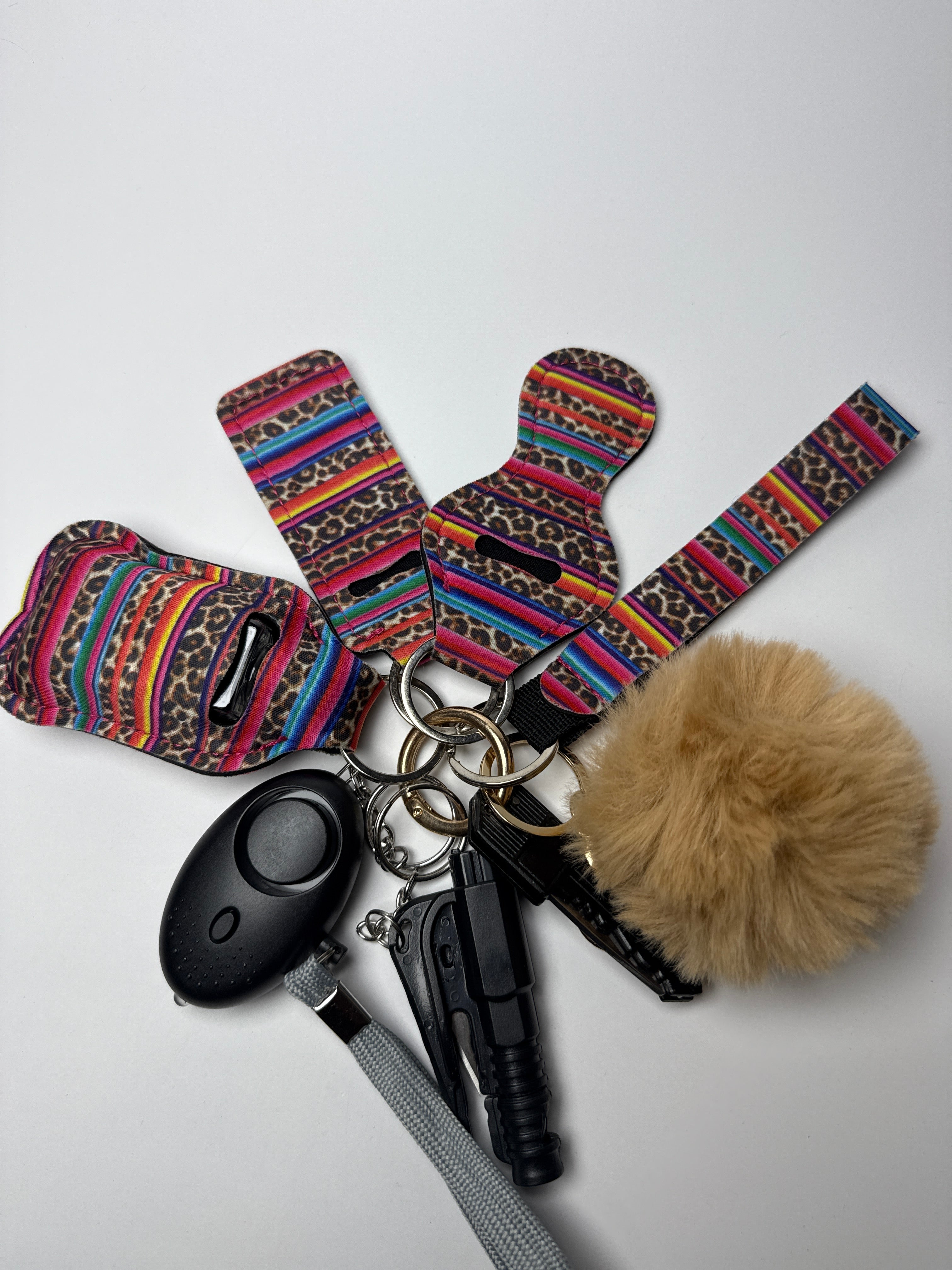 Colorful striped wristlet keychain set with tan pom charm, compact personal alarm, and mini light on a white background.