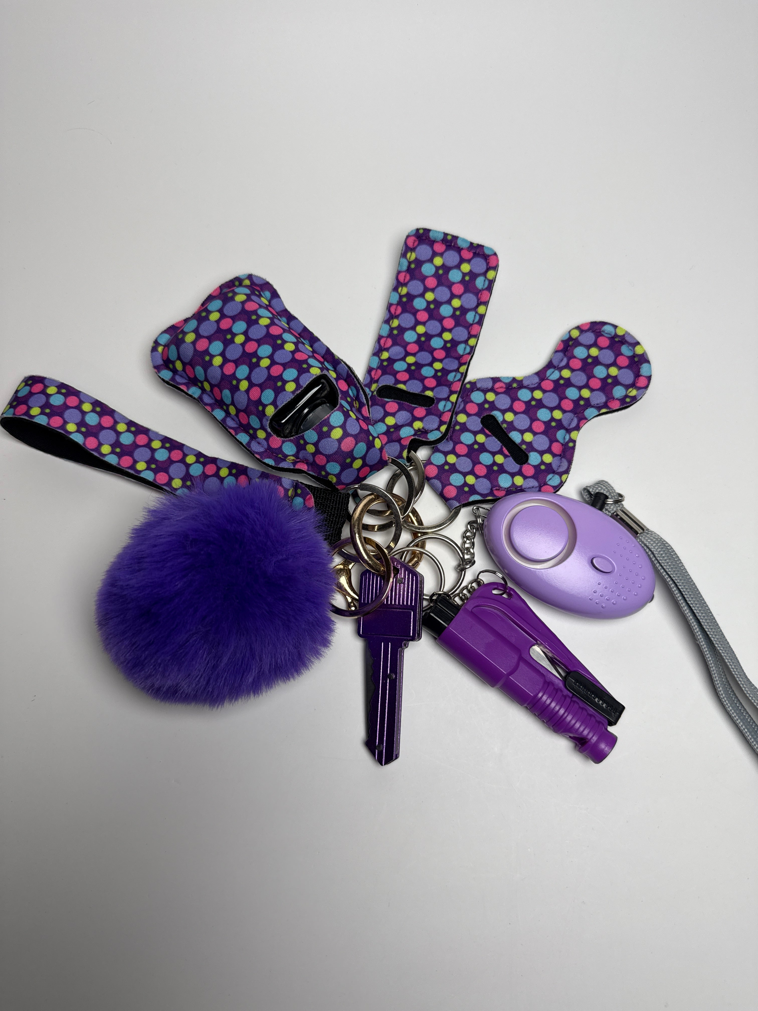 Confetti dot wristlet keychain set with purple pom charm, compact personal alarm, and mini light on a white background.