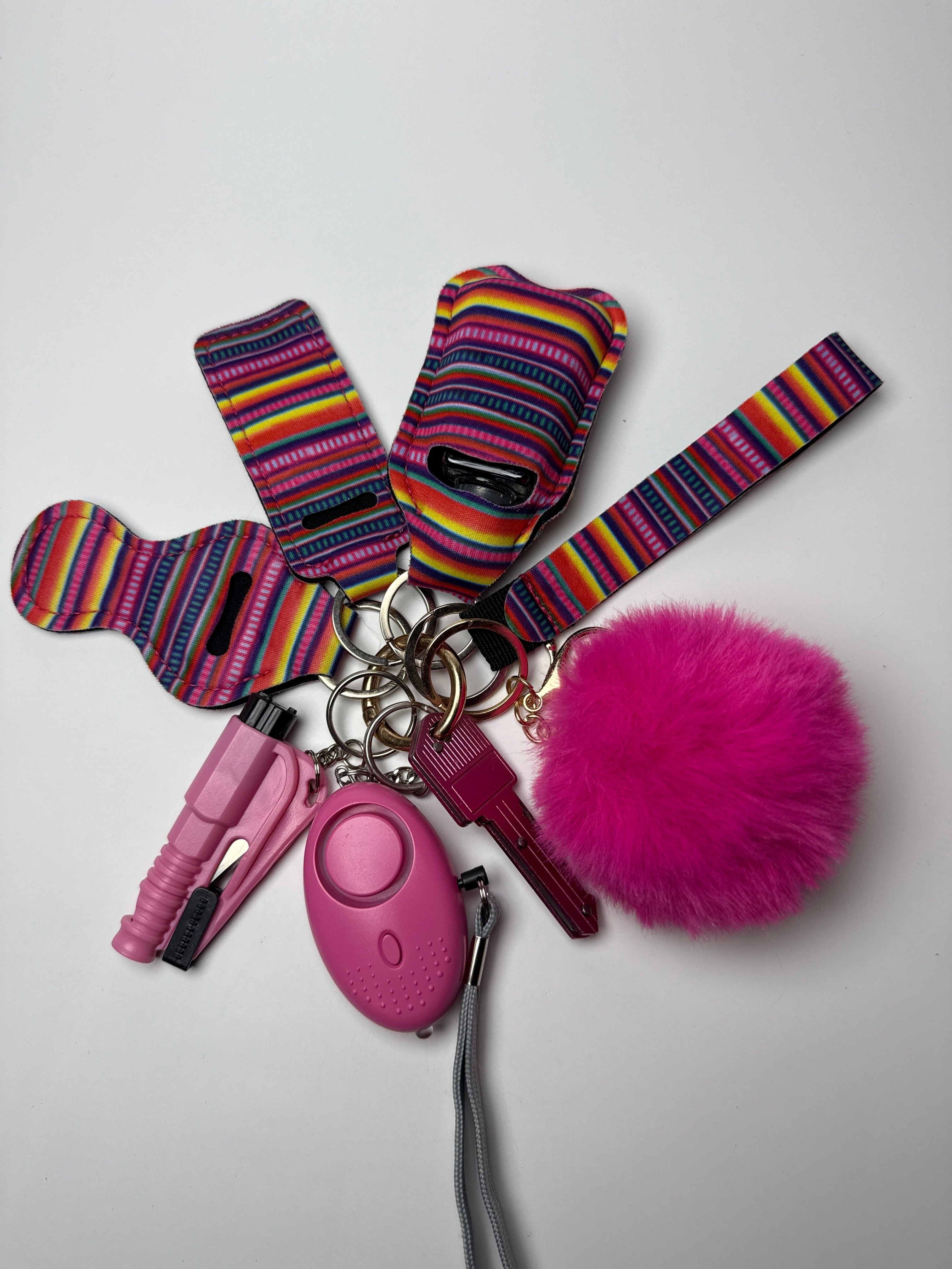 Multicolor striped wristlet keychain set with hot pink pom charm, compact personal alarm, and mini light on a white background.