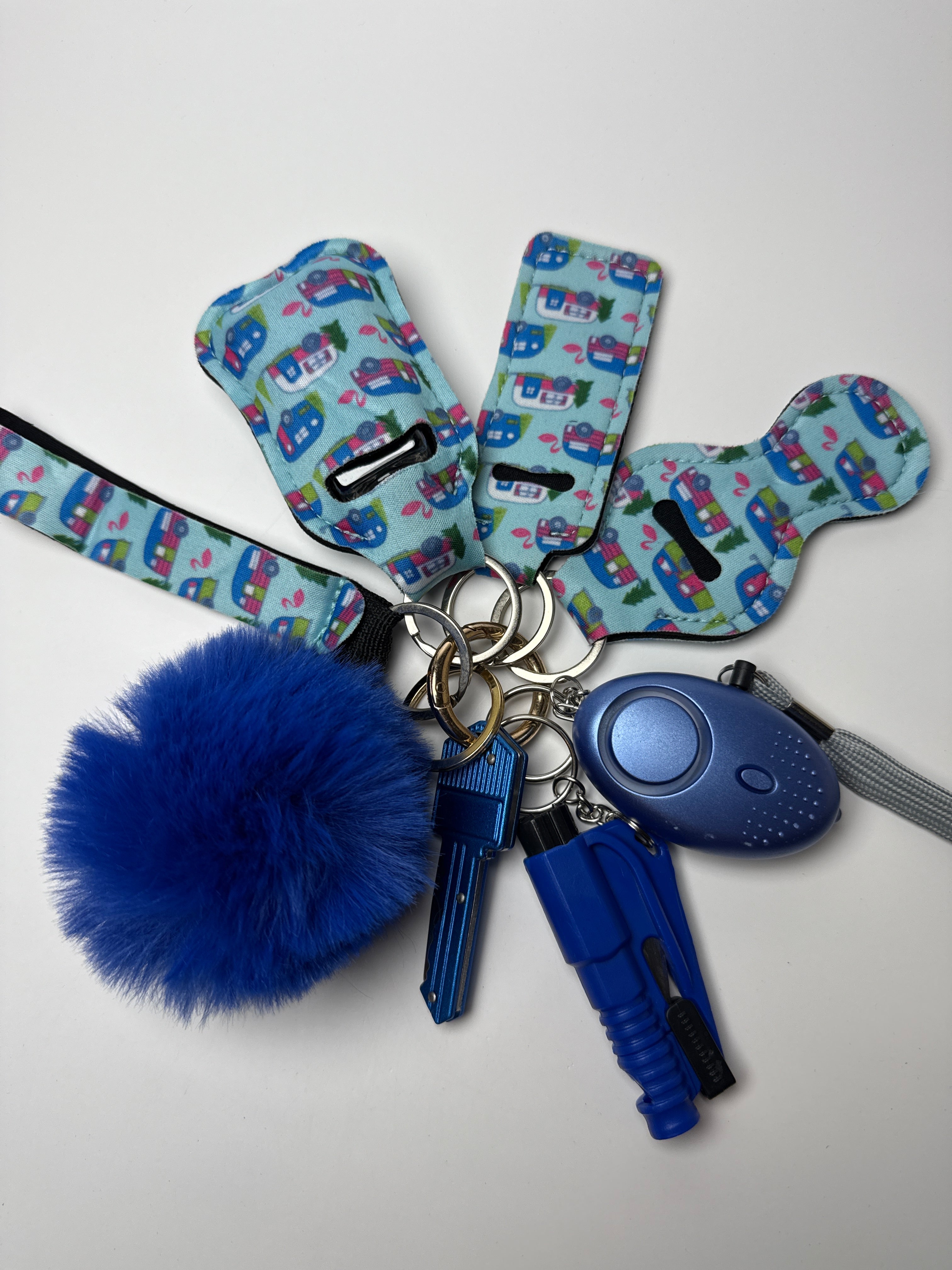 Blue camper-print wristlet keychain set with fluffy blue pom charm, compact personal alarm, and mini light on a white background.