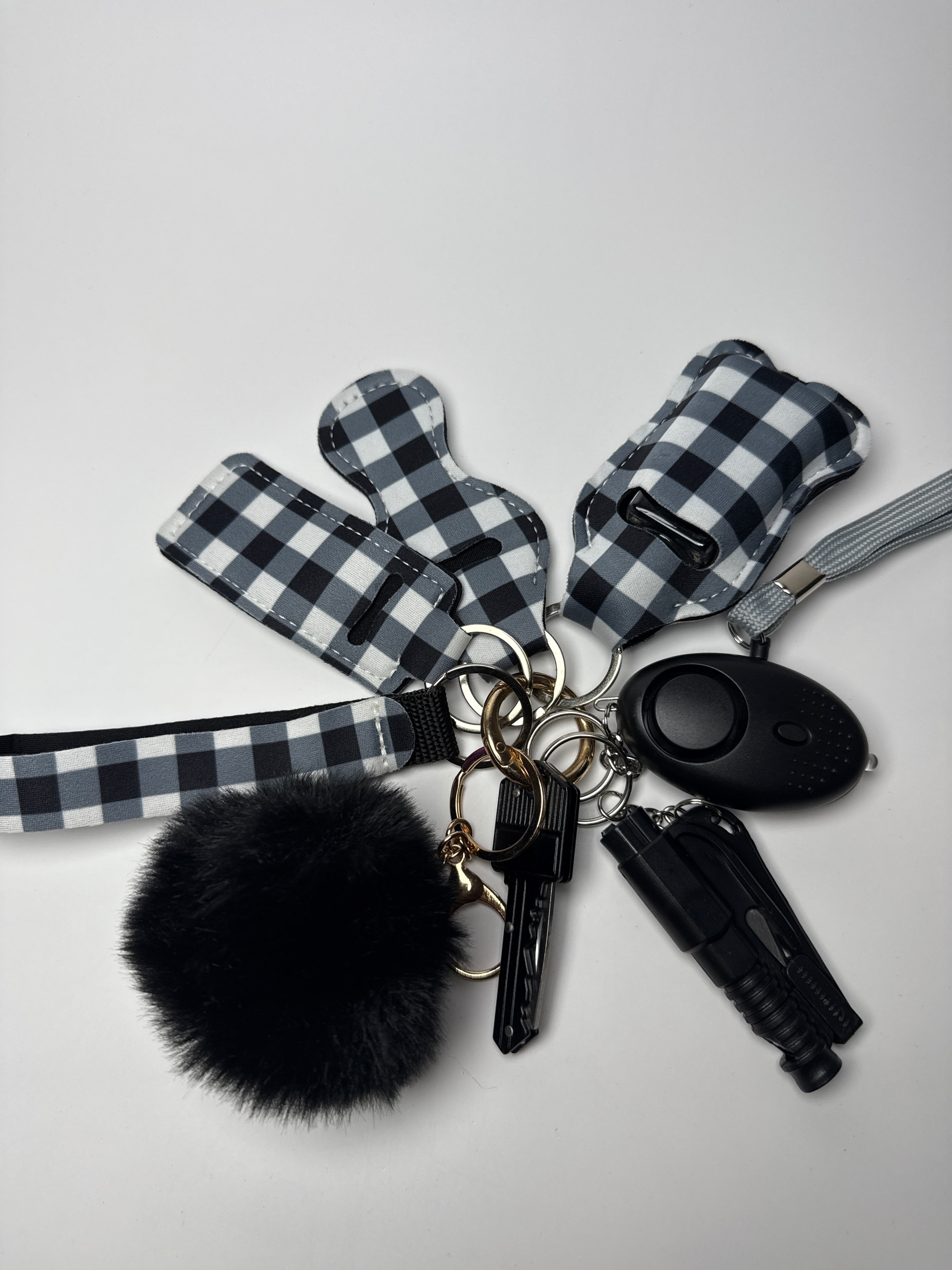 Black and white gingham wristlet keychain set with black pom charm, compact personal alarm, and mini light on a white background