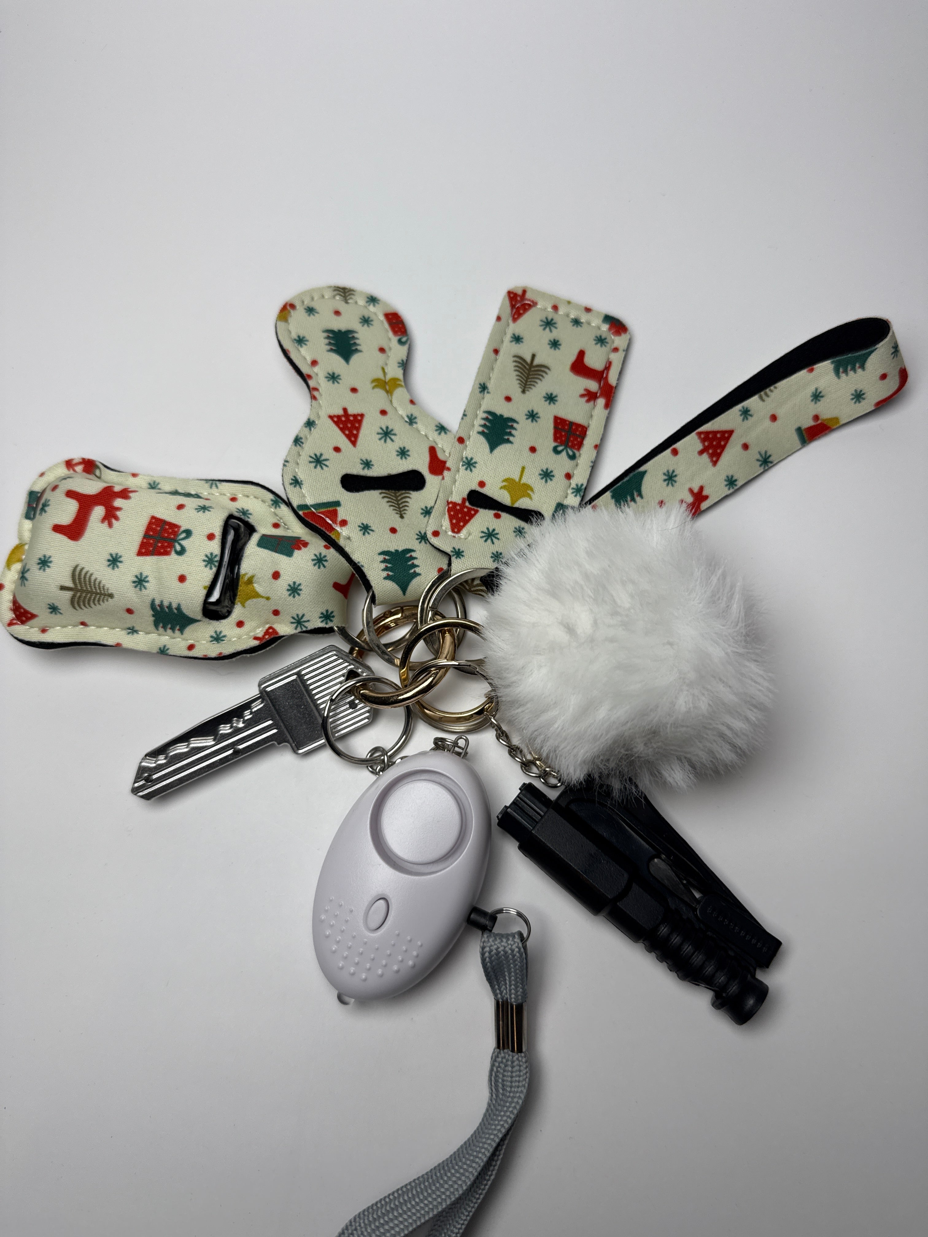 Holiday icons wristlet keychain set with white pom charm, compact personal alarm, and mini light on a white background