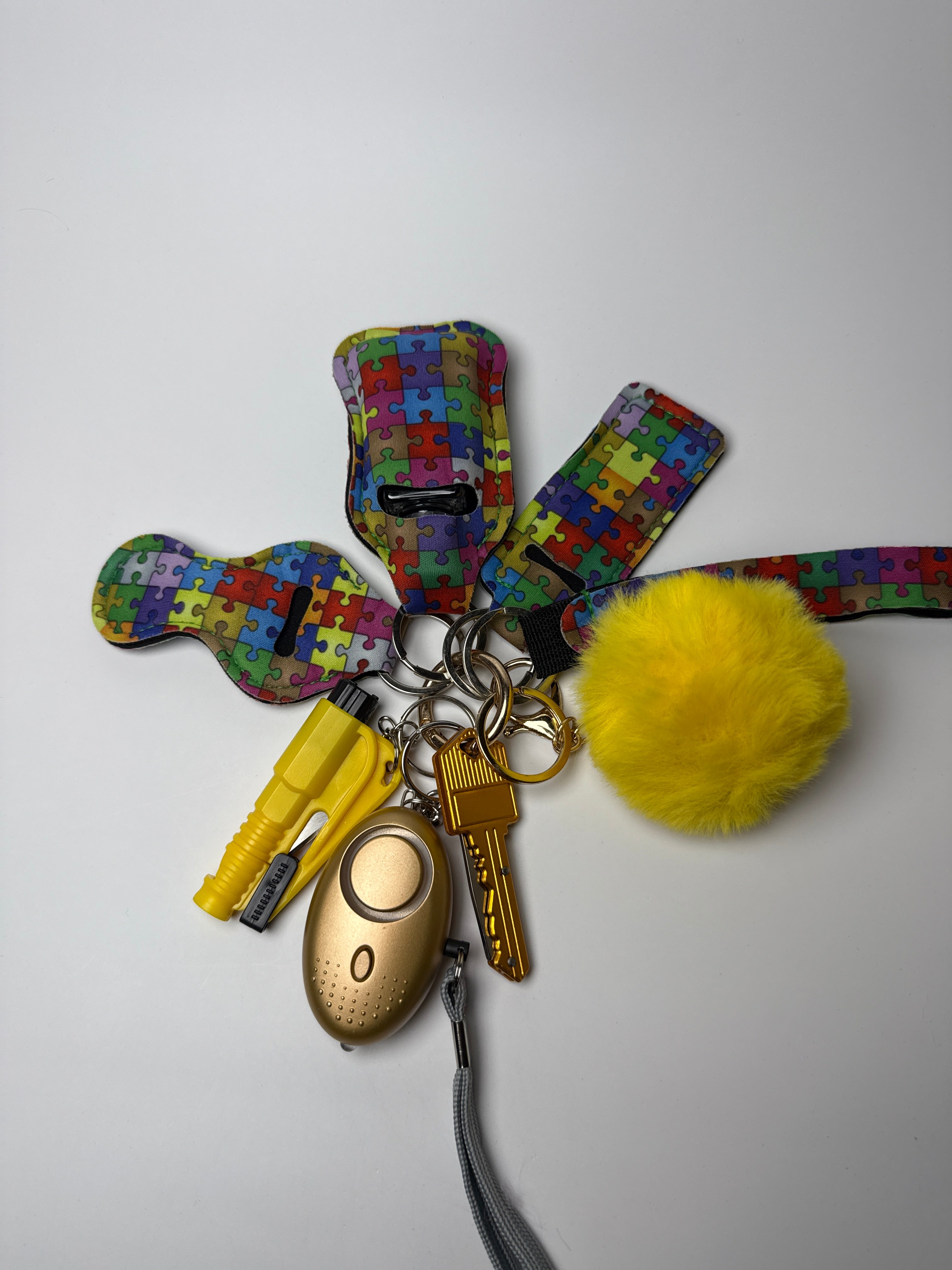 Colorful puzzle-print wristlet keychain set with yellow pom charm, compact personal alarm, and mini light on a white background.