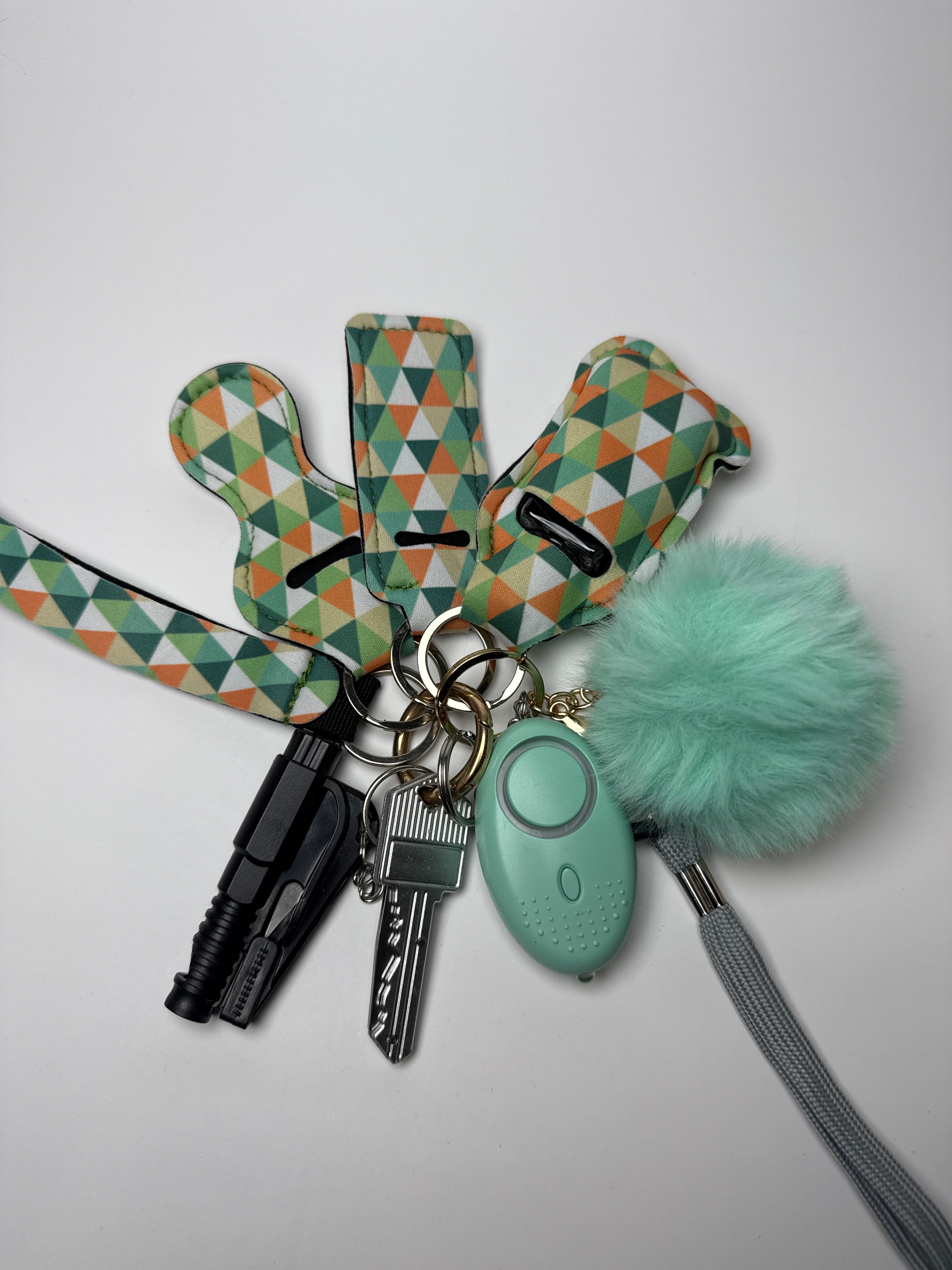 Triangle print wristlet keychain set with mint pom charm, compact personal alarm, and mini light on a white background.