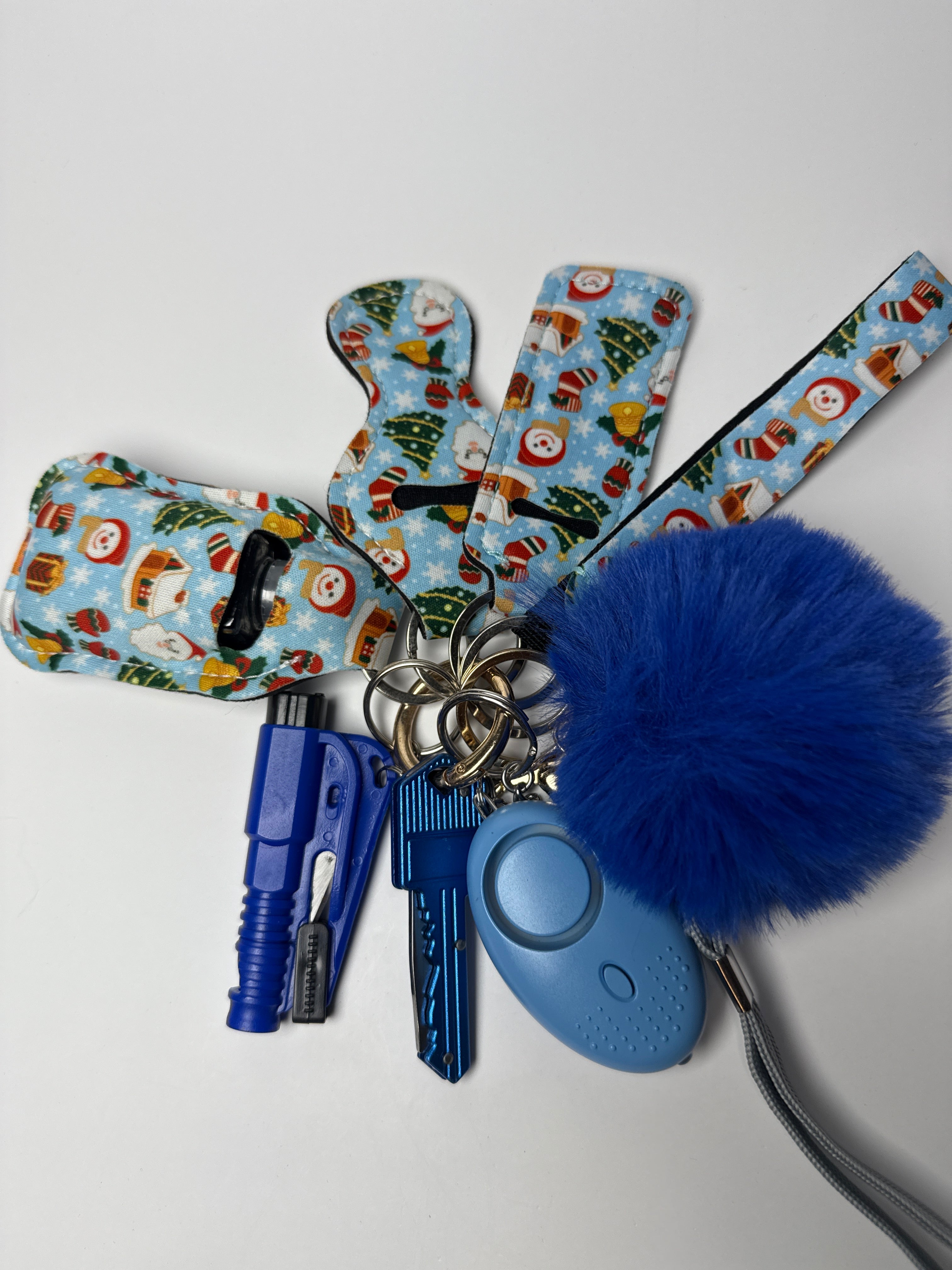 Holiday print wristlet keychain set with blue pom charm, compact personal alarm, and mini light on a white background.