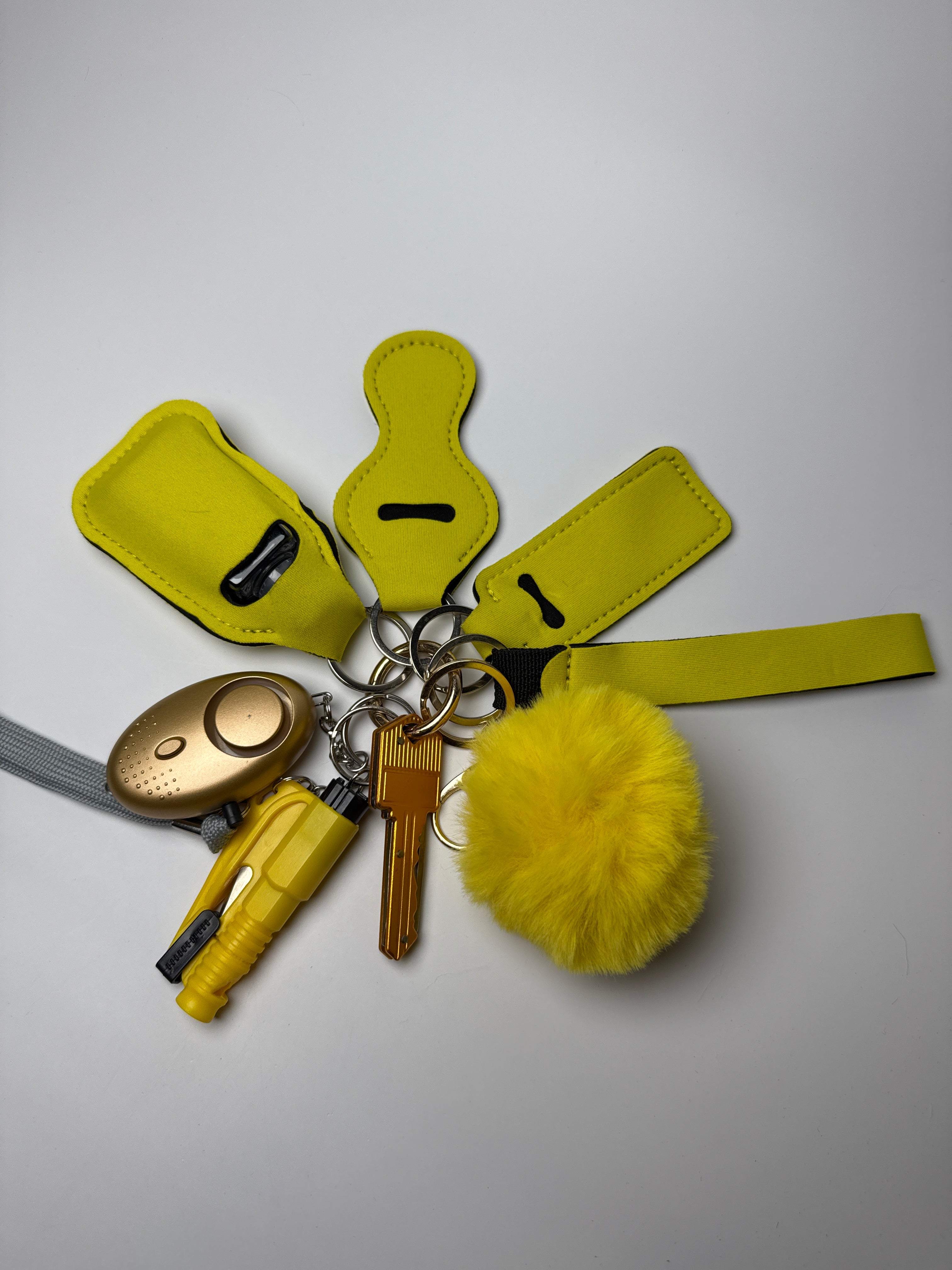 Solid yellow wristlet keychain set with yellow pom charm, compact personal alarm, and mini light on a white background.