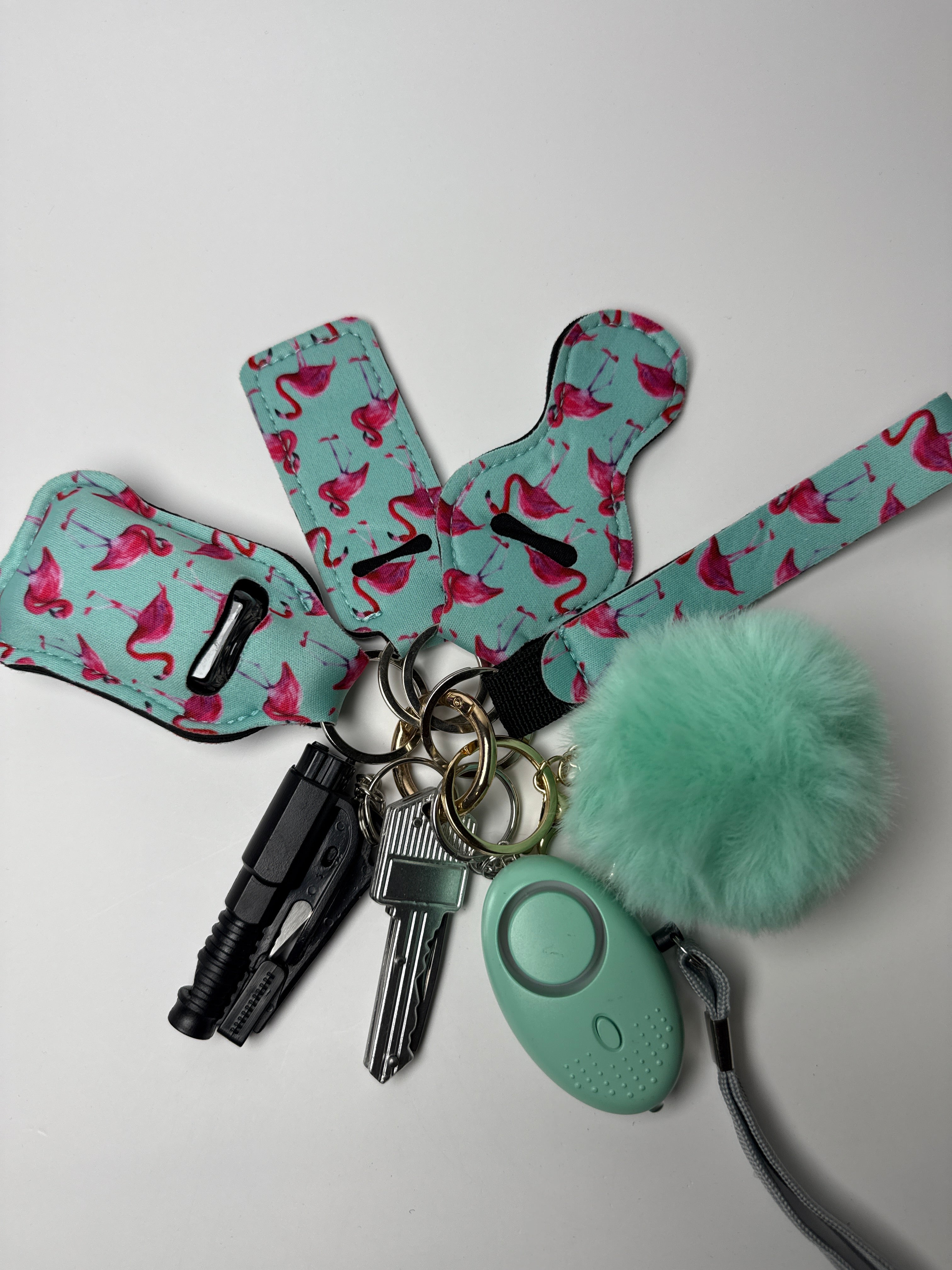 Flamingo-print wristlet keychain set with mint pom charm, compact personal alarm, and mini light on a white background