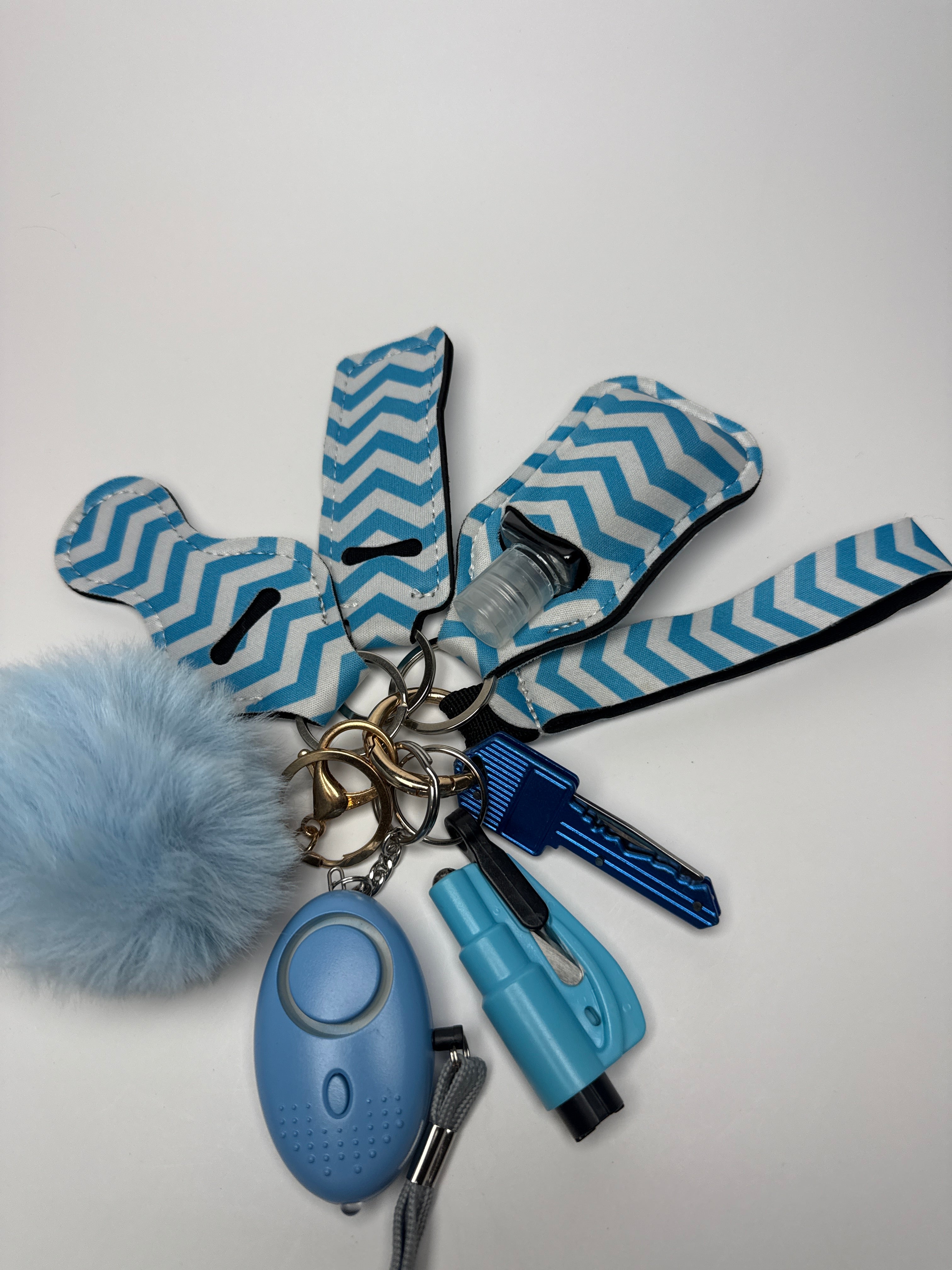 Blue and white chevron wristlet keychain set with light blue pom charm, compact personal alarm, mini light, and a small clip-on bottle/holder on a white background.