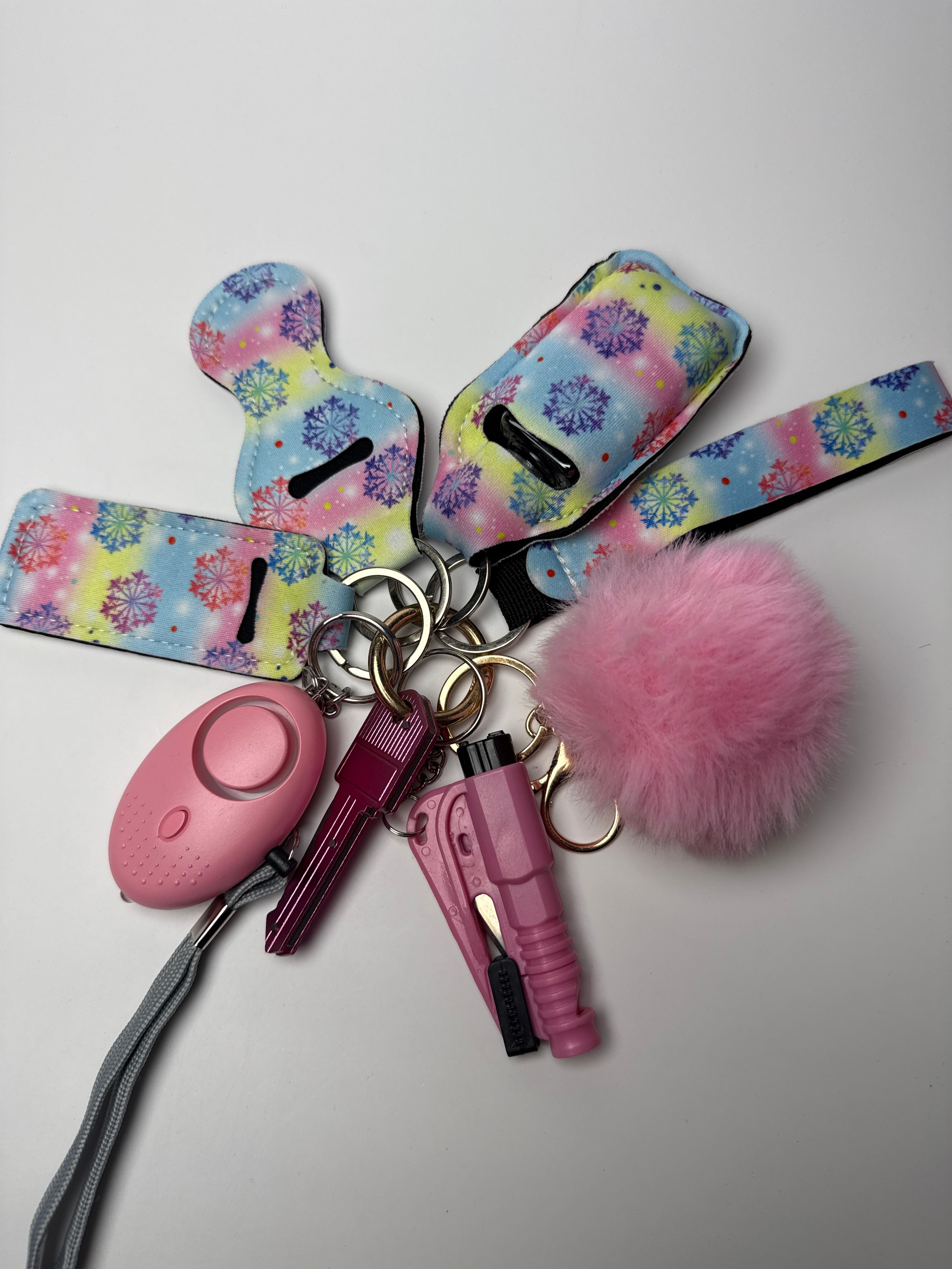 Pastel snowflake wristlet keychain set with pink pom charm, compact personal alarm, and mini light on a white background.