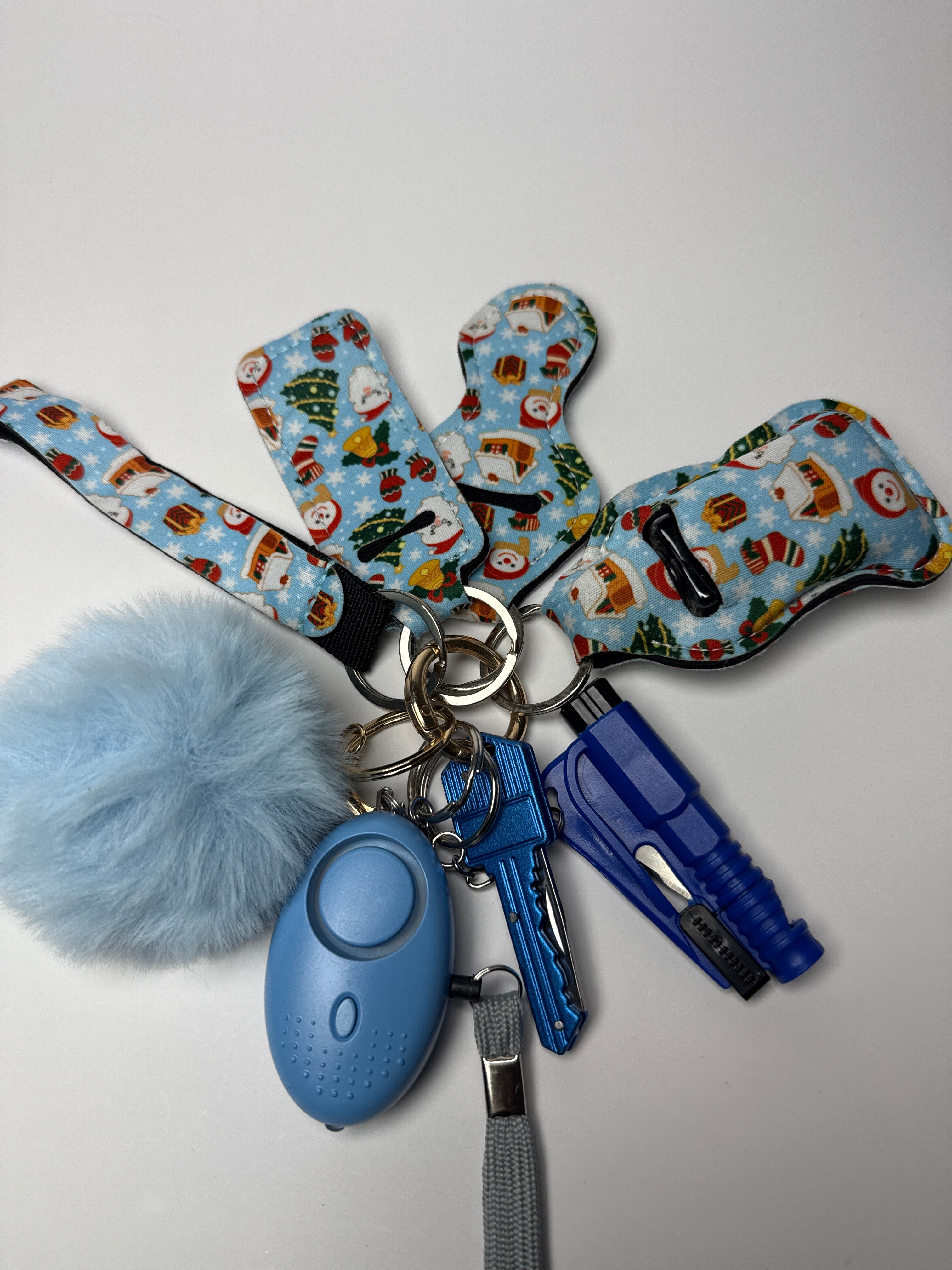 Holiday print wristlet keychain set with light blue pom charm, compact personal alarm, and mini light on a white background.