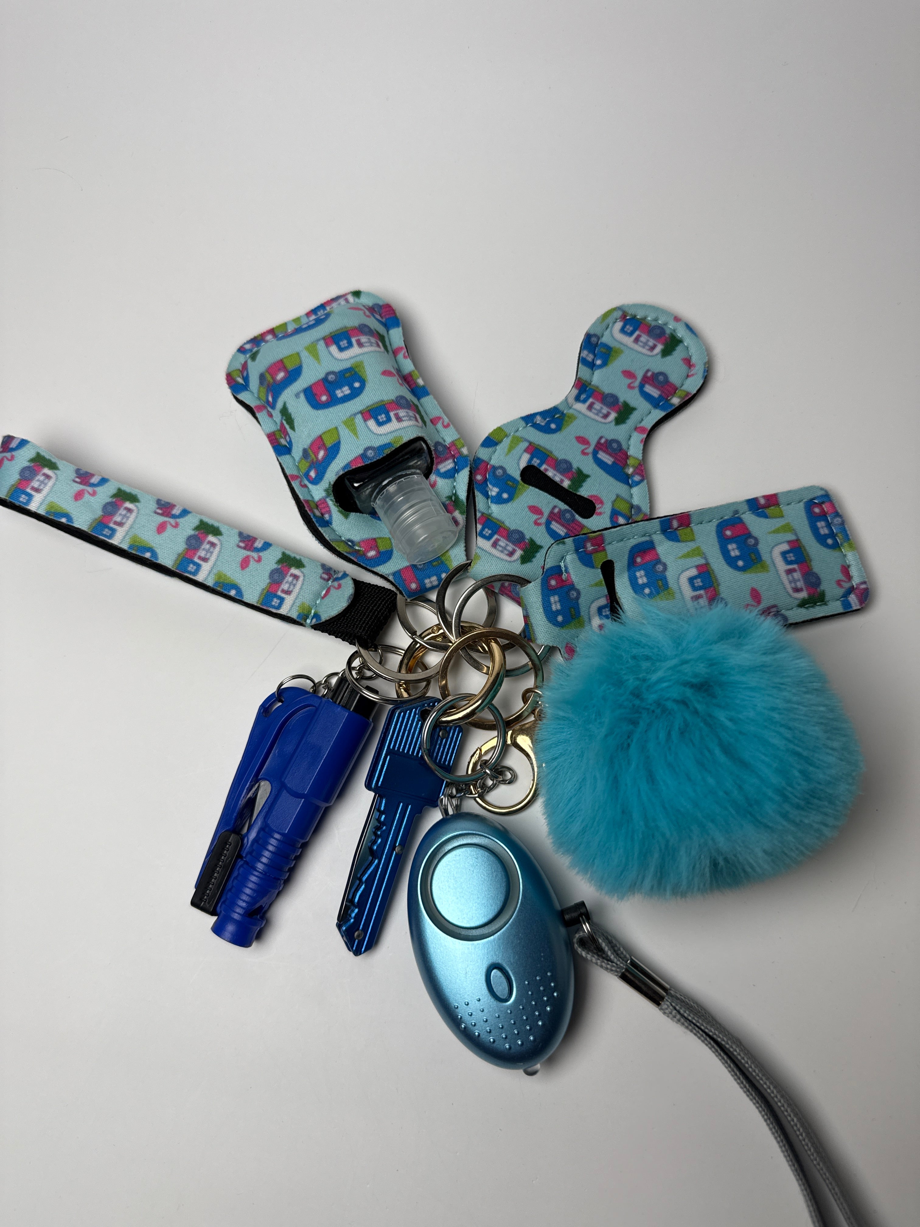 Blue camper-print wristlet keychain set with fluffy blue pom charm, compact personal alarm, and mini light on a white background.