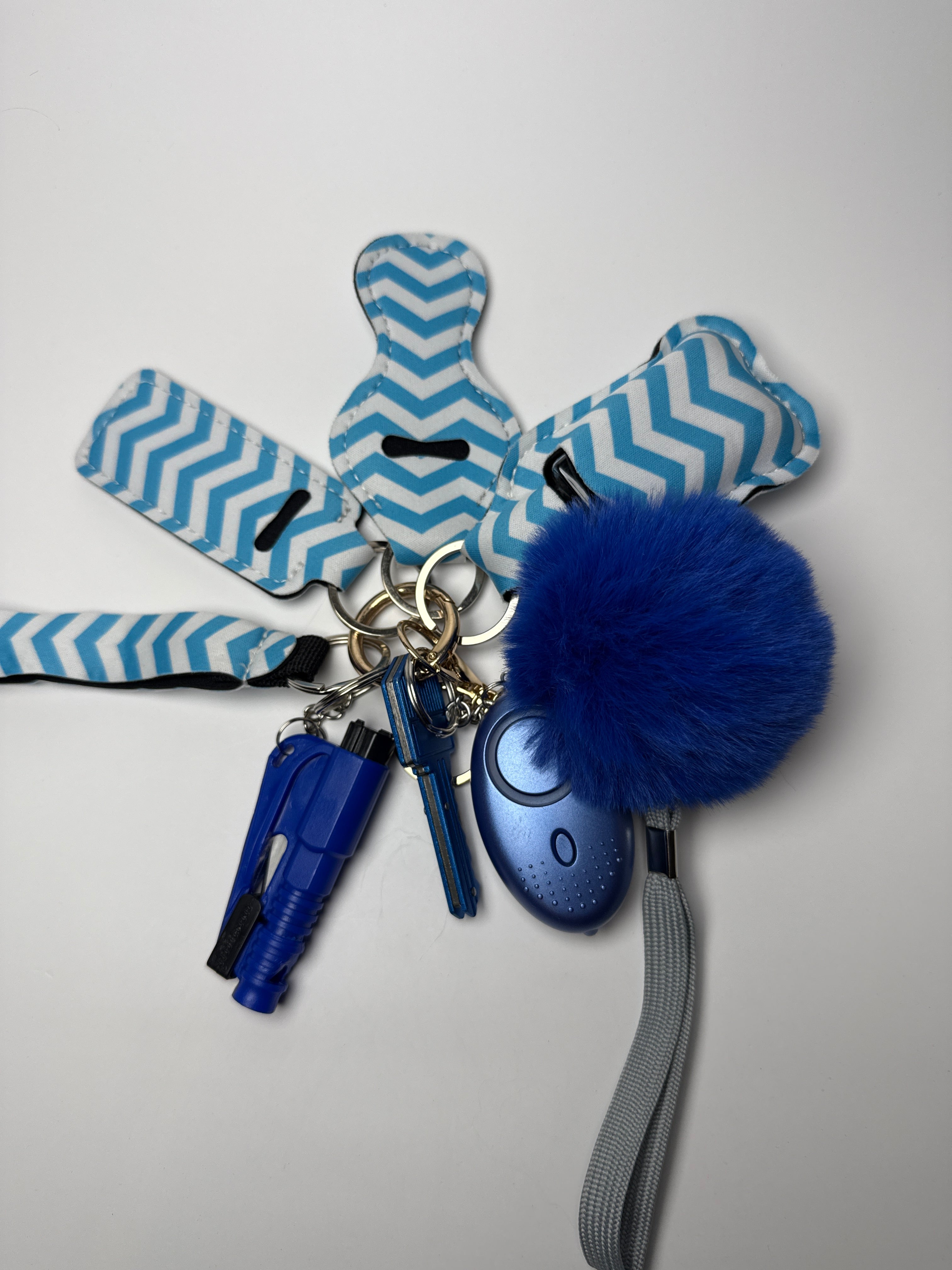 Blue and white chevron wristlet keychain set with fluffy blue pom charm, compact personal alarm, and mini light on a white background.