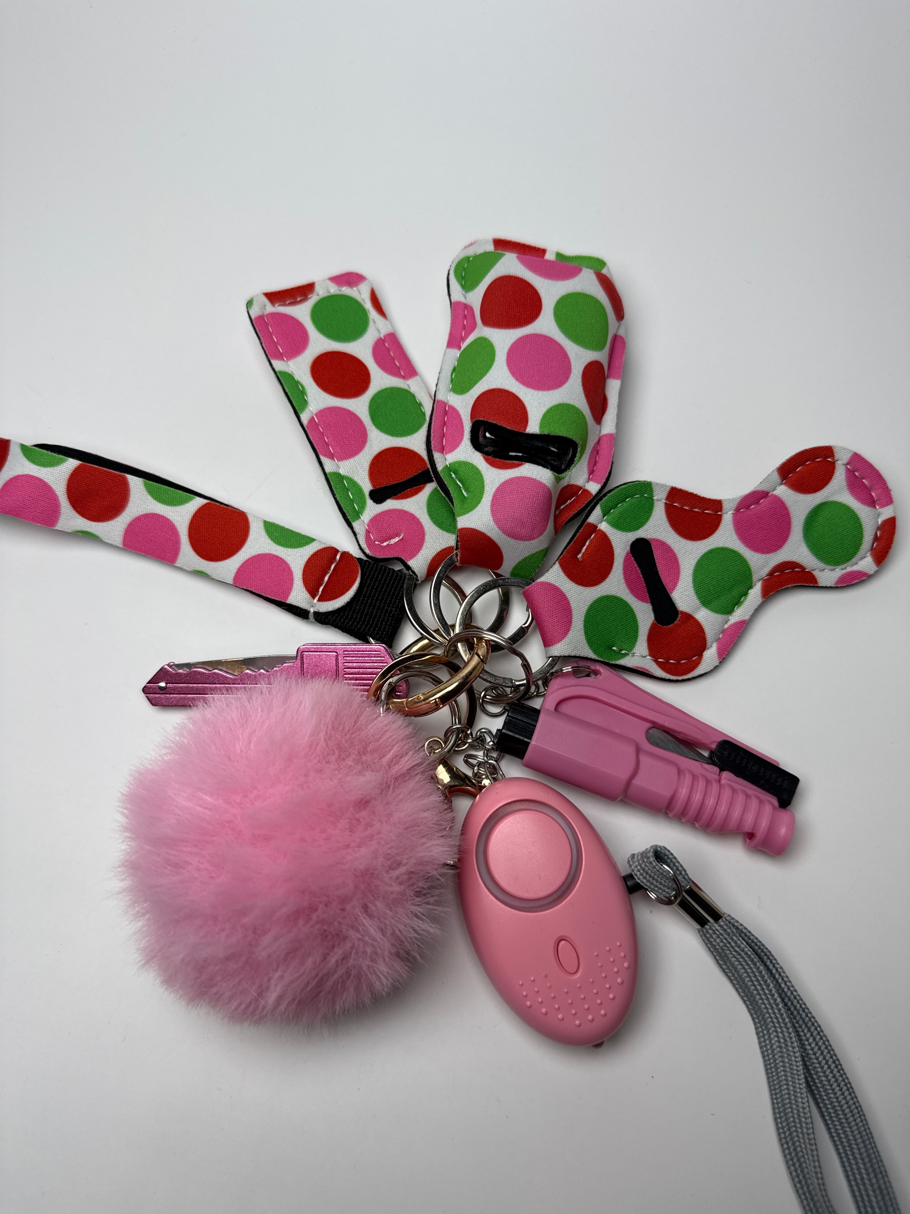 Colorful polka dot wristlet keychain set with fluffy pink pom charm, compact personal alarm, and mini light on a white background.