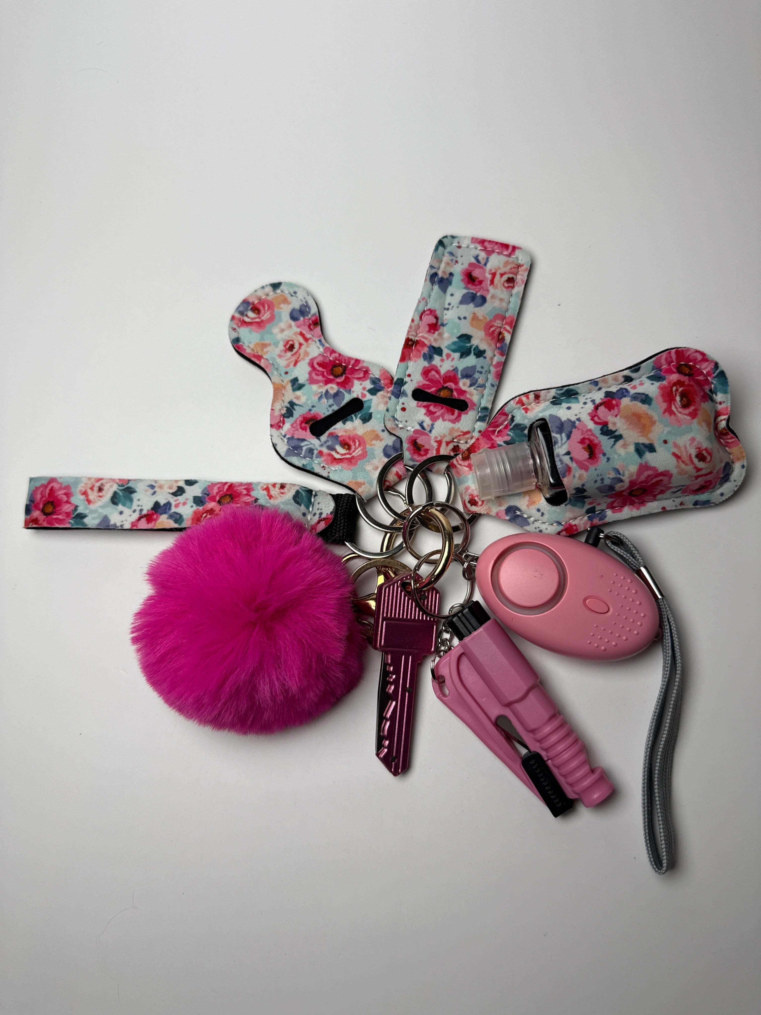 Floral wristlet keychain set with hot pink pom charm, compact personal alarm, and mini light on a white background.