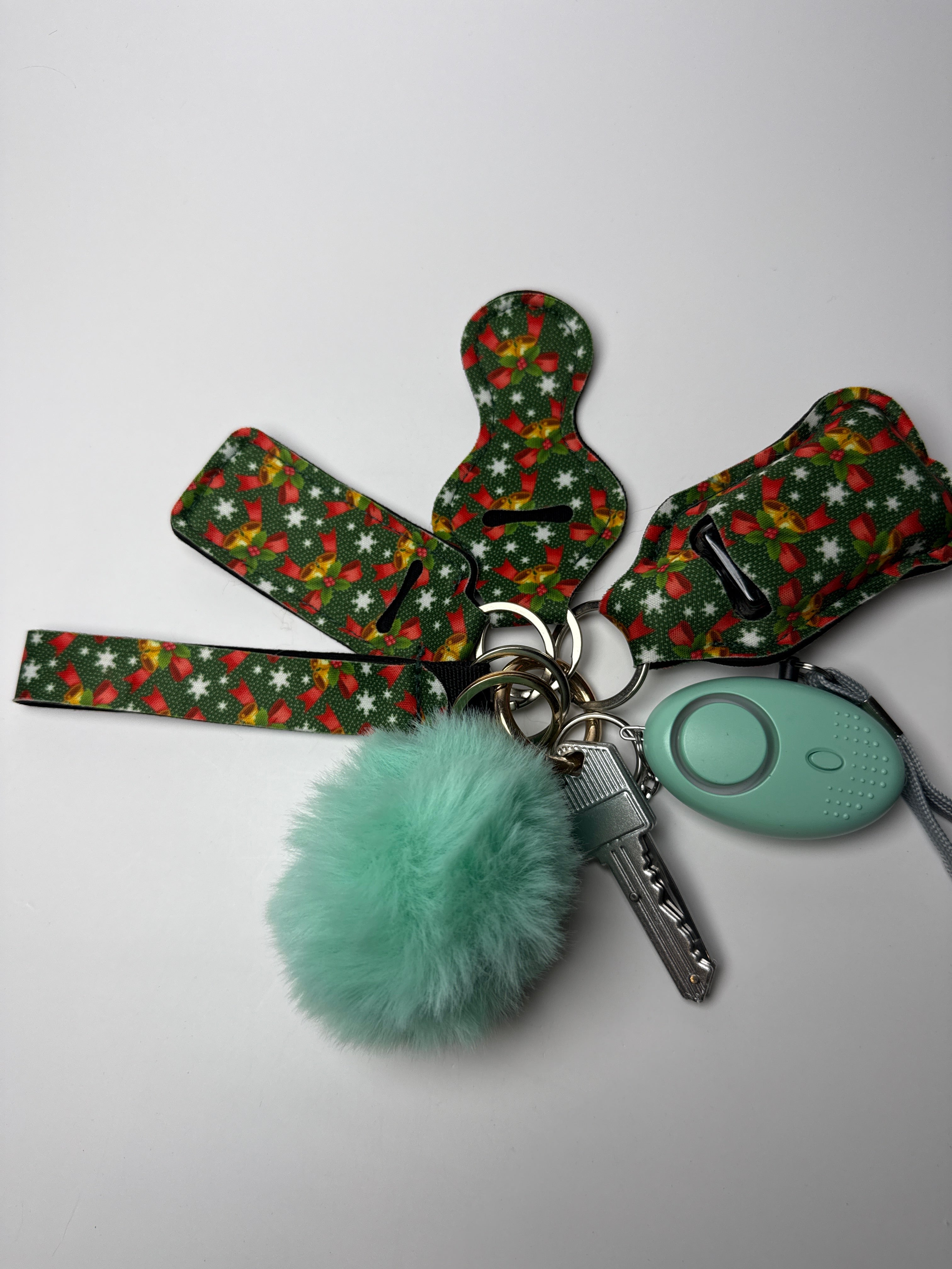 Holly print wristlet keychain set with mint pom charm and compact personal alarm on a white background.