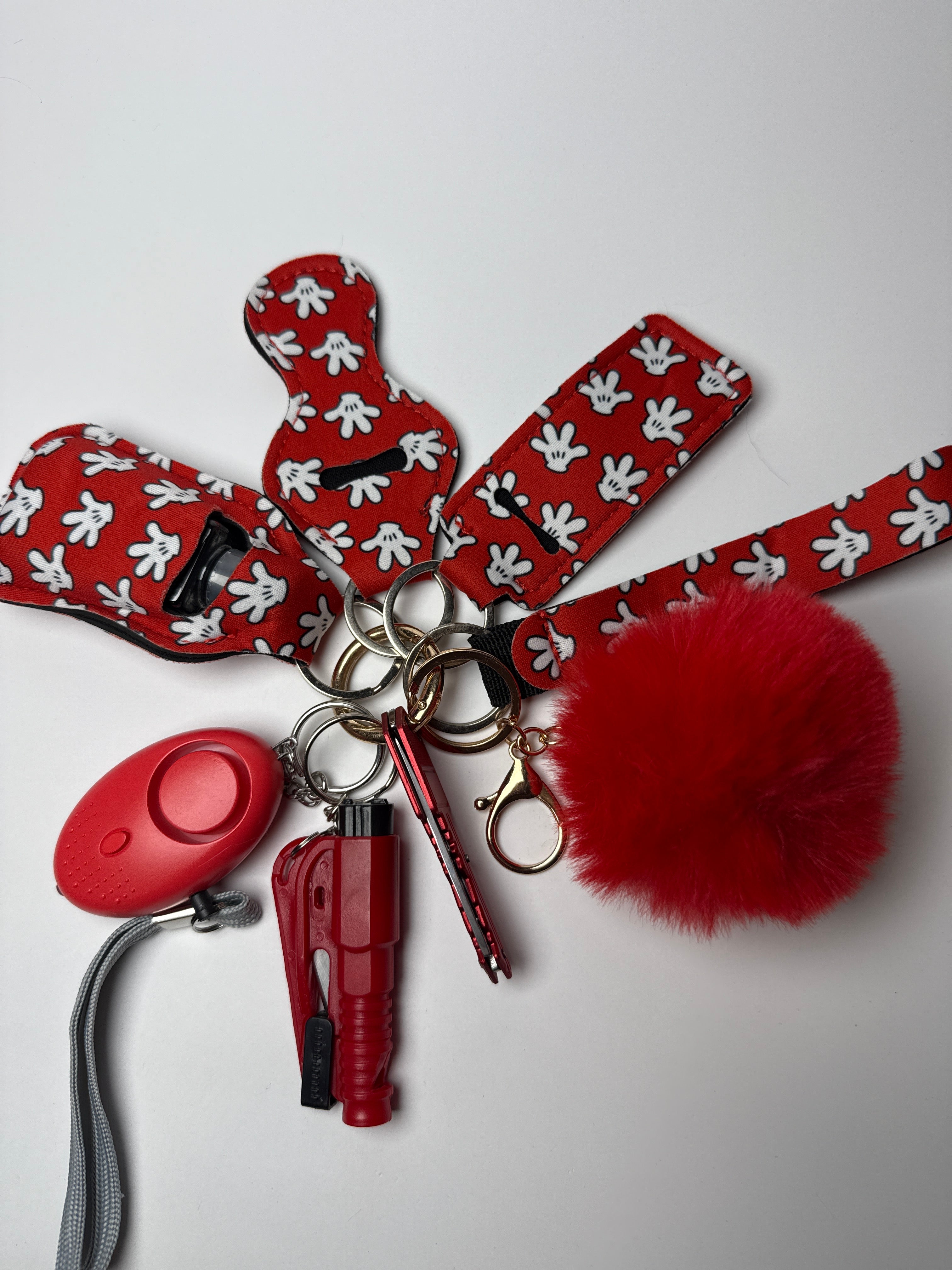 Red wristlet keychain set with white glove-print straps, red pom charm, compact personal alarm, and mini light on a white background.