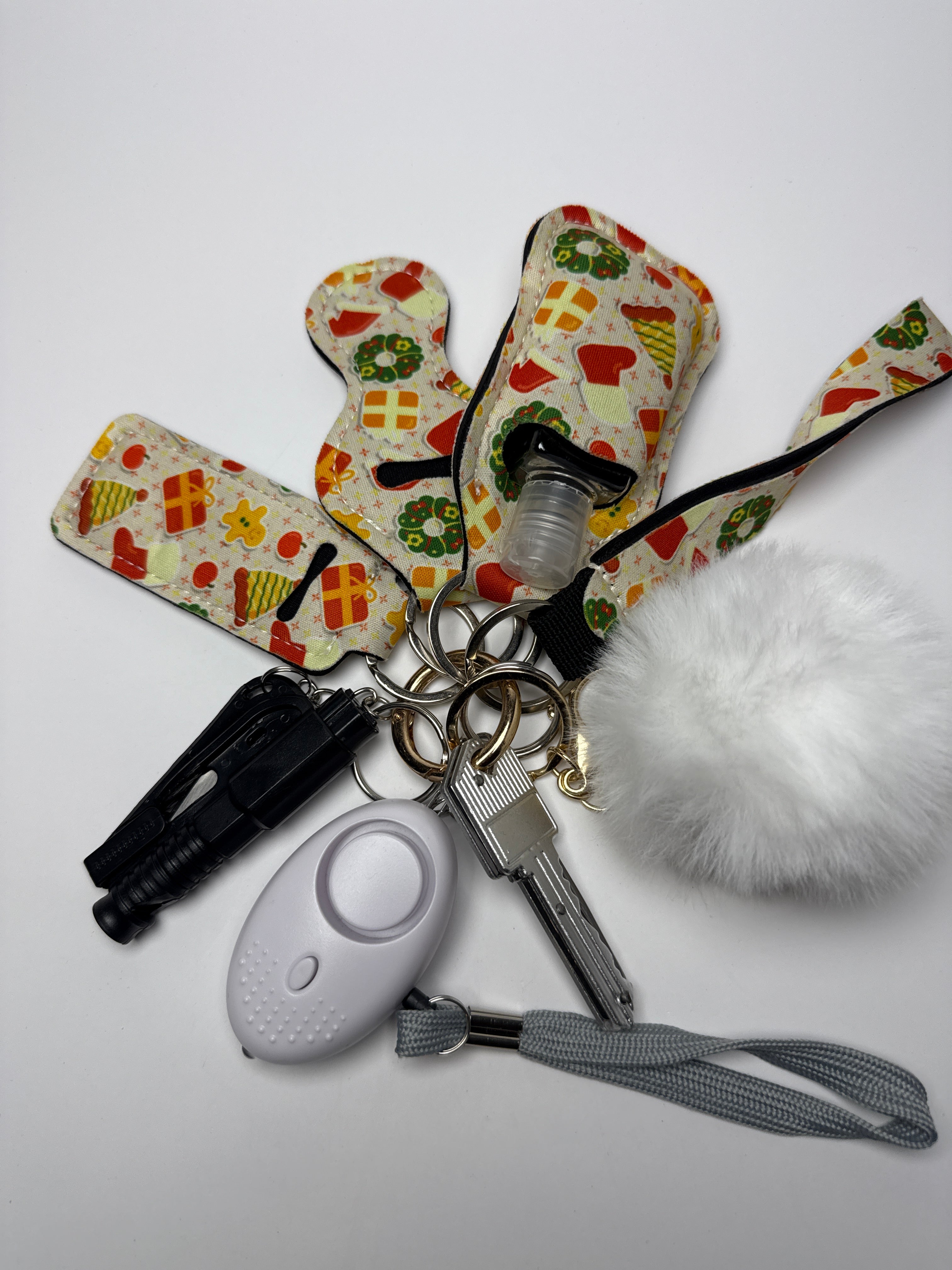 Holiday Gifts wristlet keychain set with white pom charm, compact personal alarm, mini light, and clip-on bottle/holder on a white background.