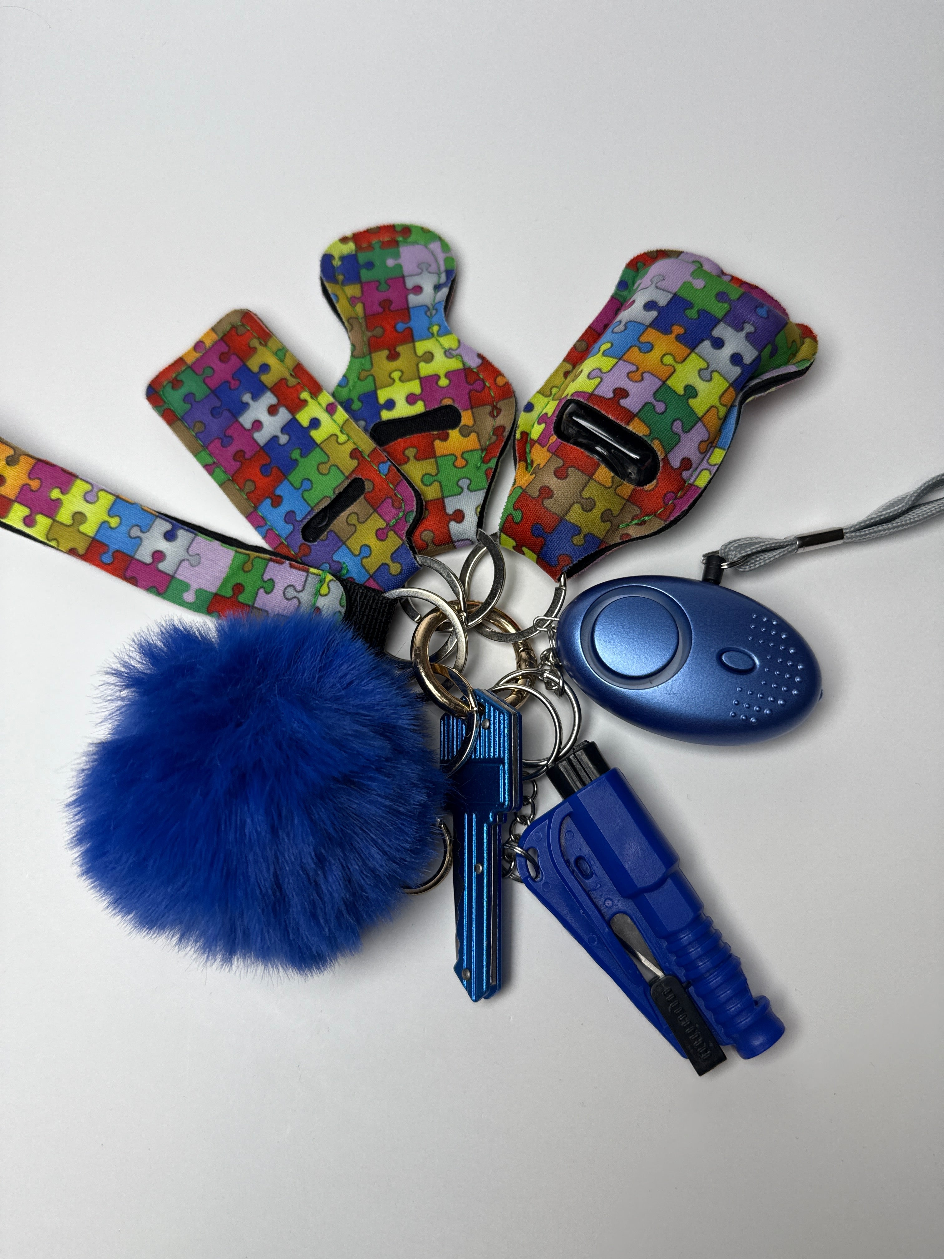 Puzzle print wristlet keychain set with blue pom charm, compact personal alarm, and mini light on a white background.
