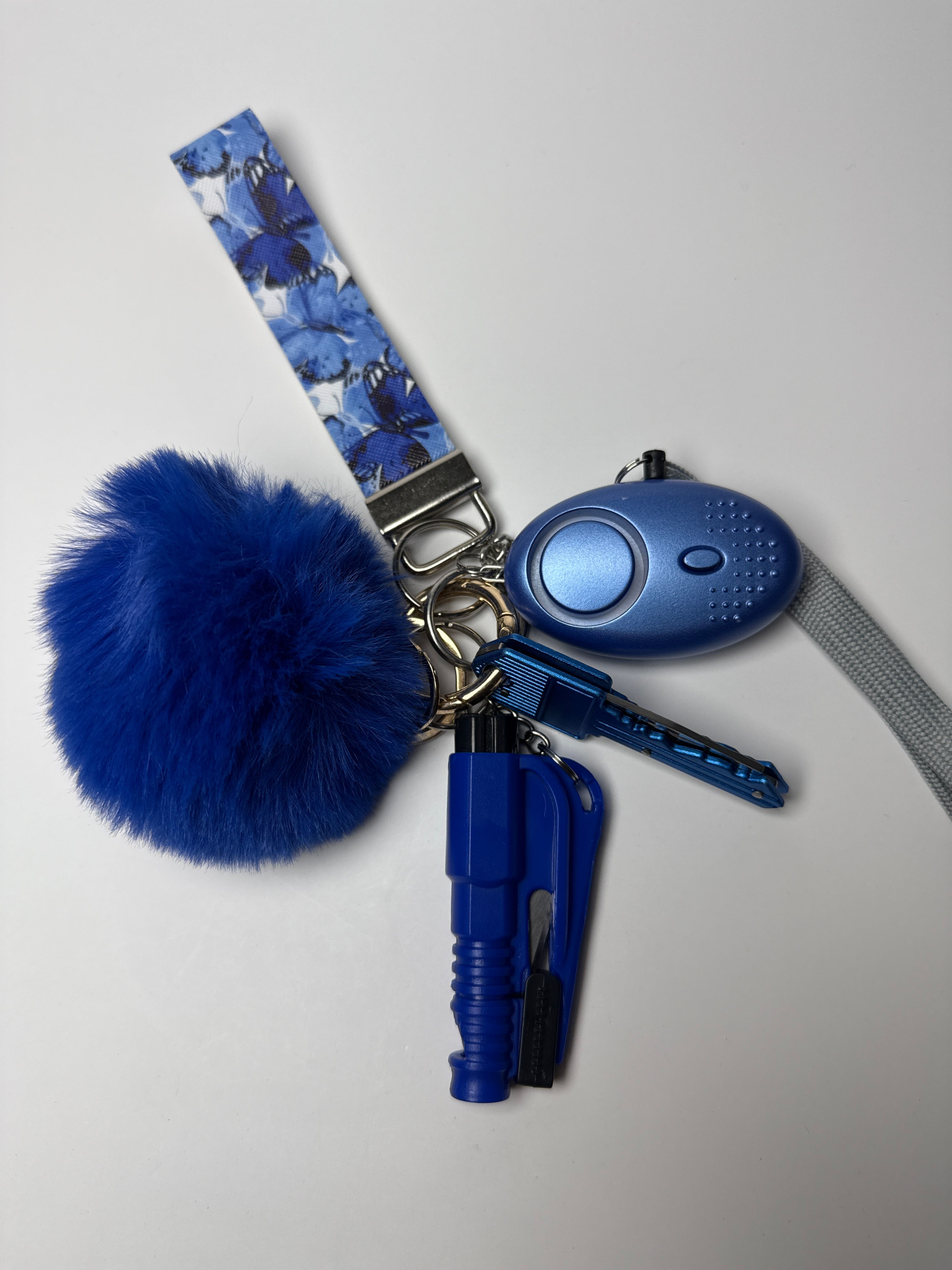 Blue floral wristlet keychain set with blue pom charm, compact personal alarm, and mini light on a white background.
