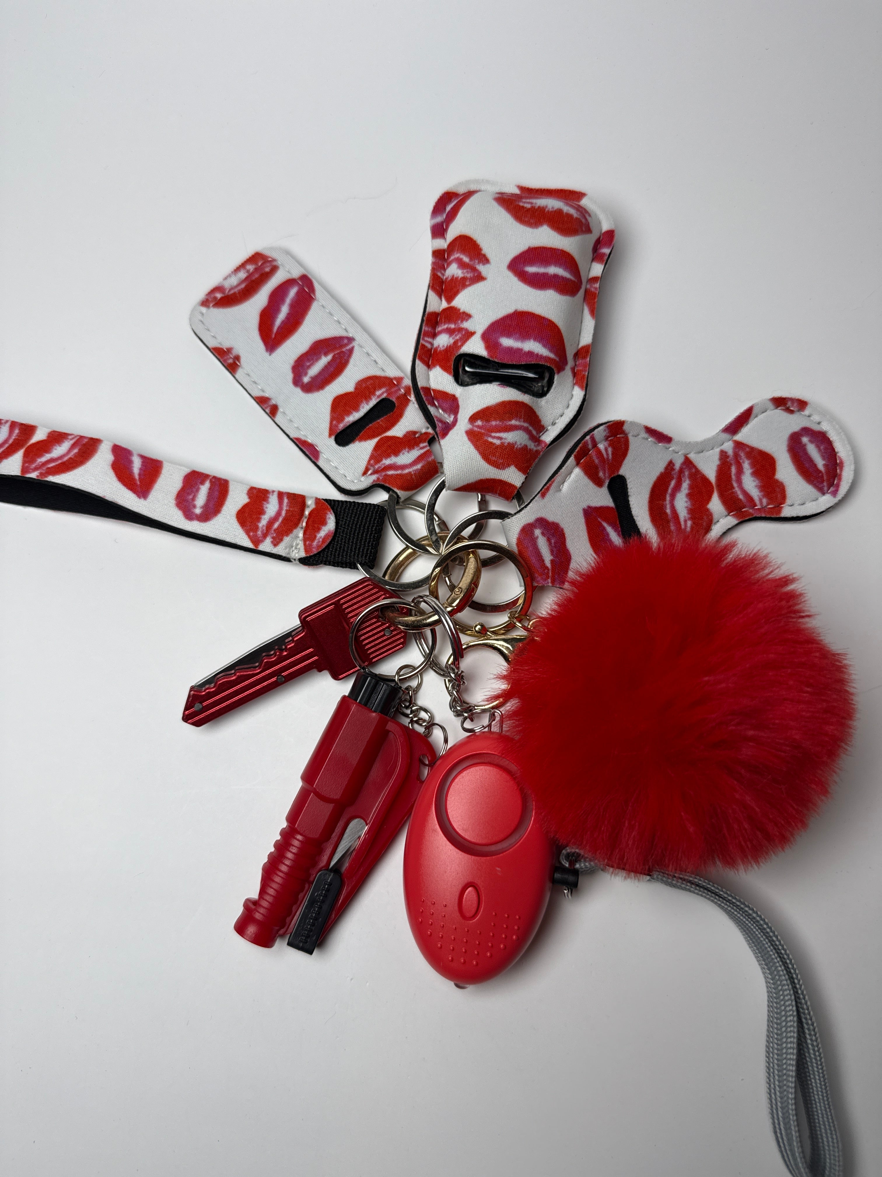 Red and white kiss-print wristlet keychain set with red pom charm, compact personal alarm, and mini light on a white background.