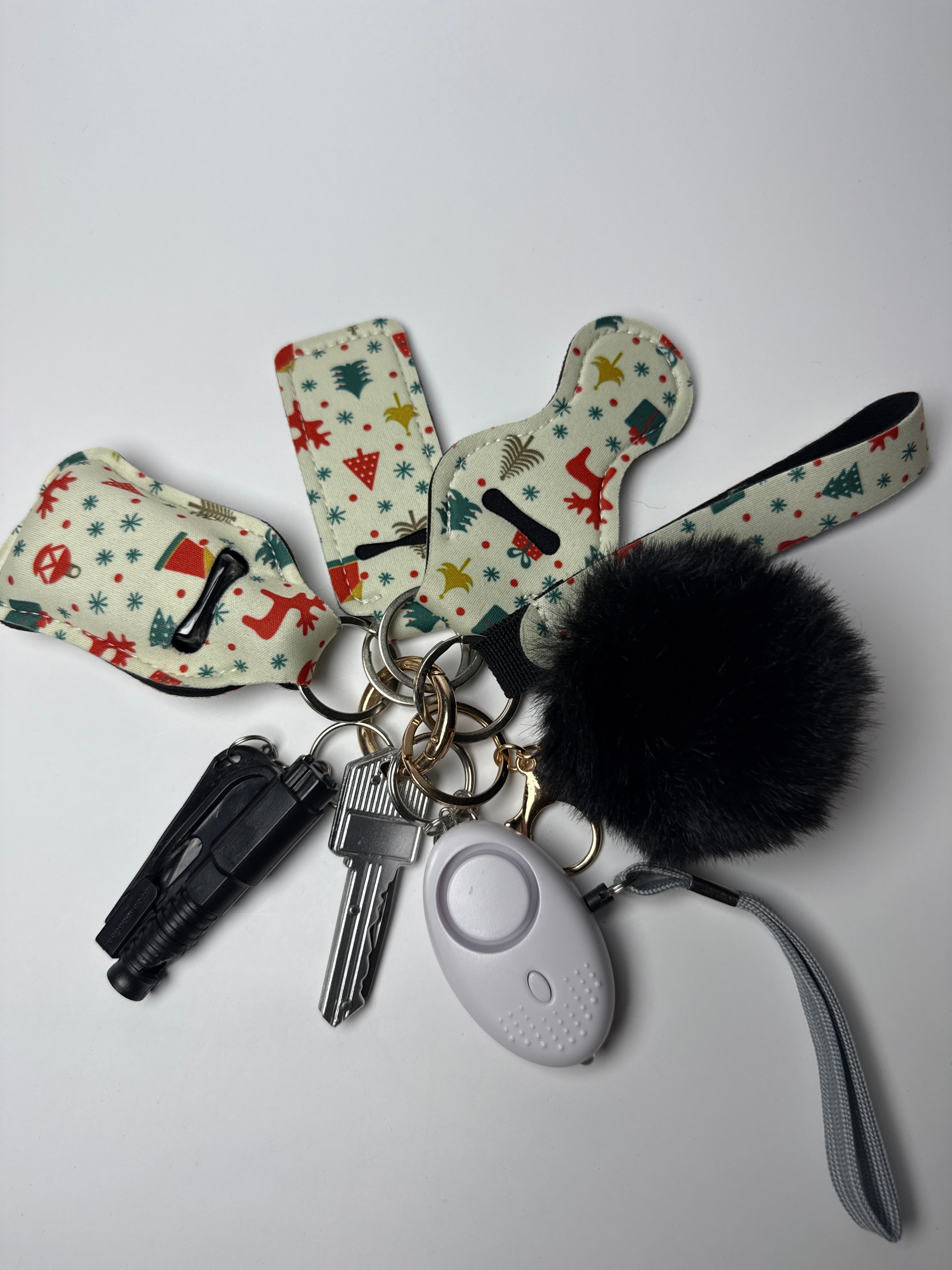 Holiday icons wristlet keychain set with black pom charm, compact personal alarm, and mini light on a white background.