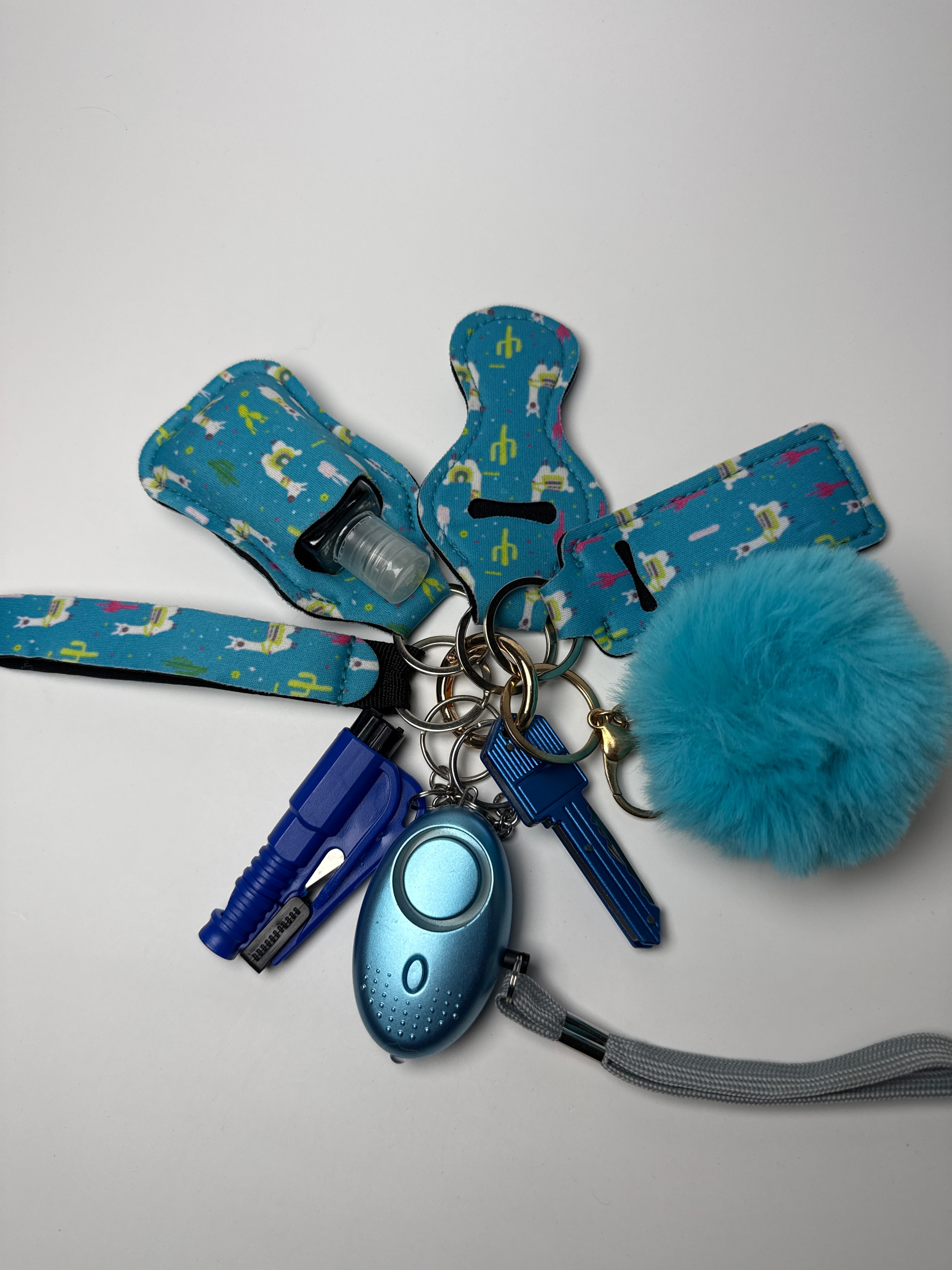 Blue llama-print wristlet keychain set with fluffy blue pom charm, compact personal alarm, and mini light on a white background.